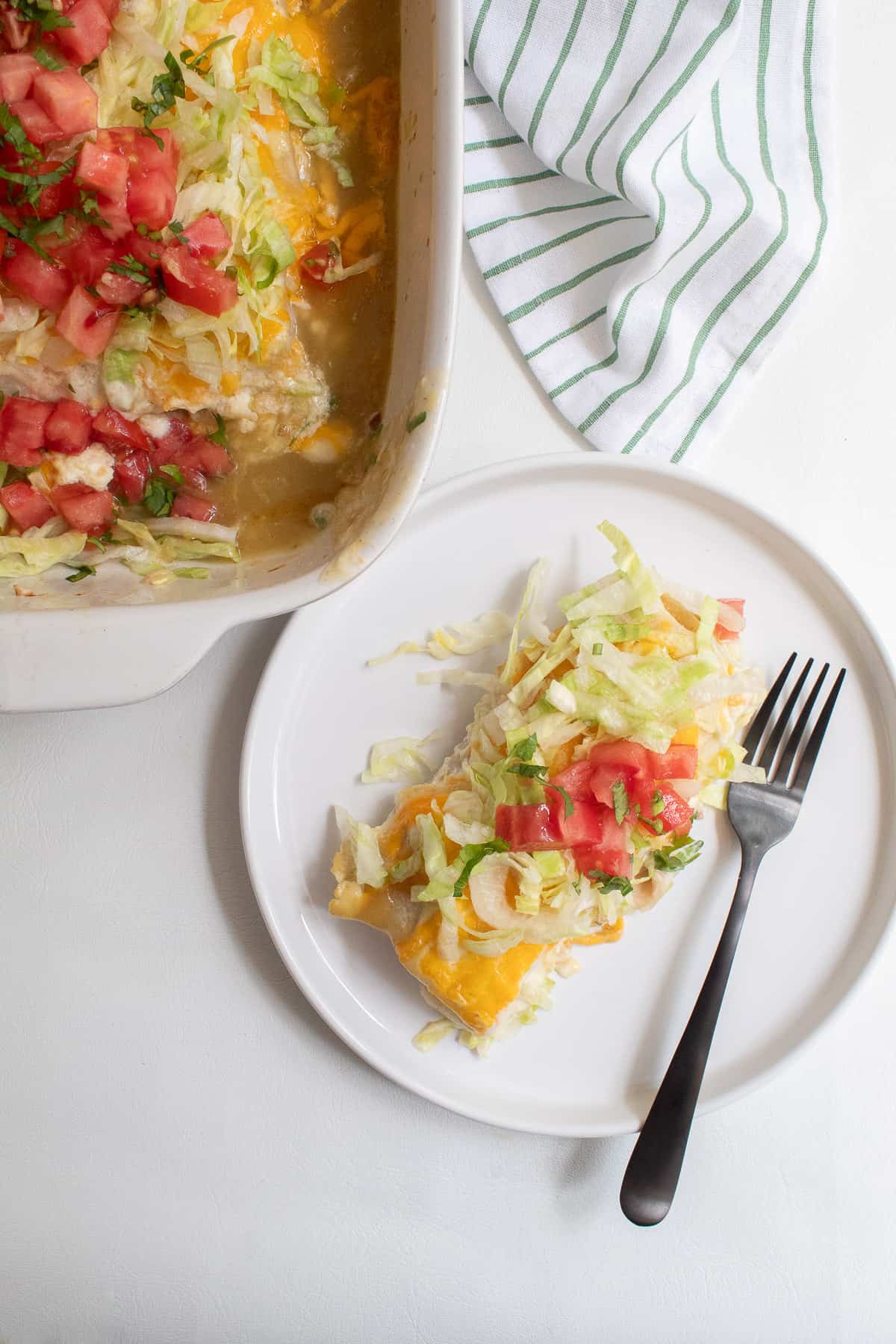 One burrito sits on a white plate next to a black fork. The casserole dish is off to the side.