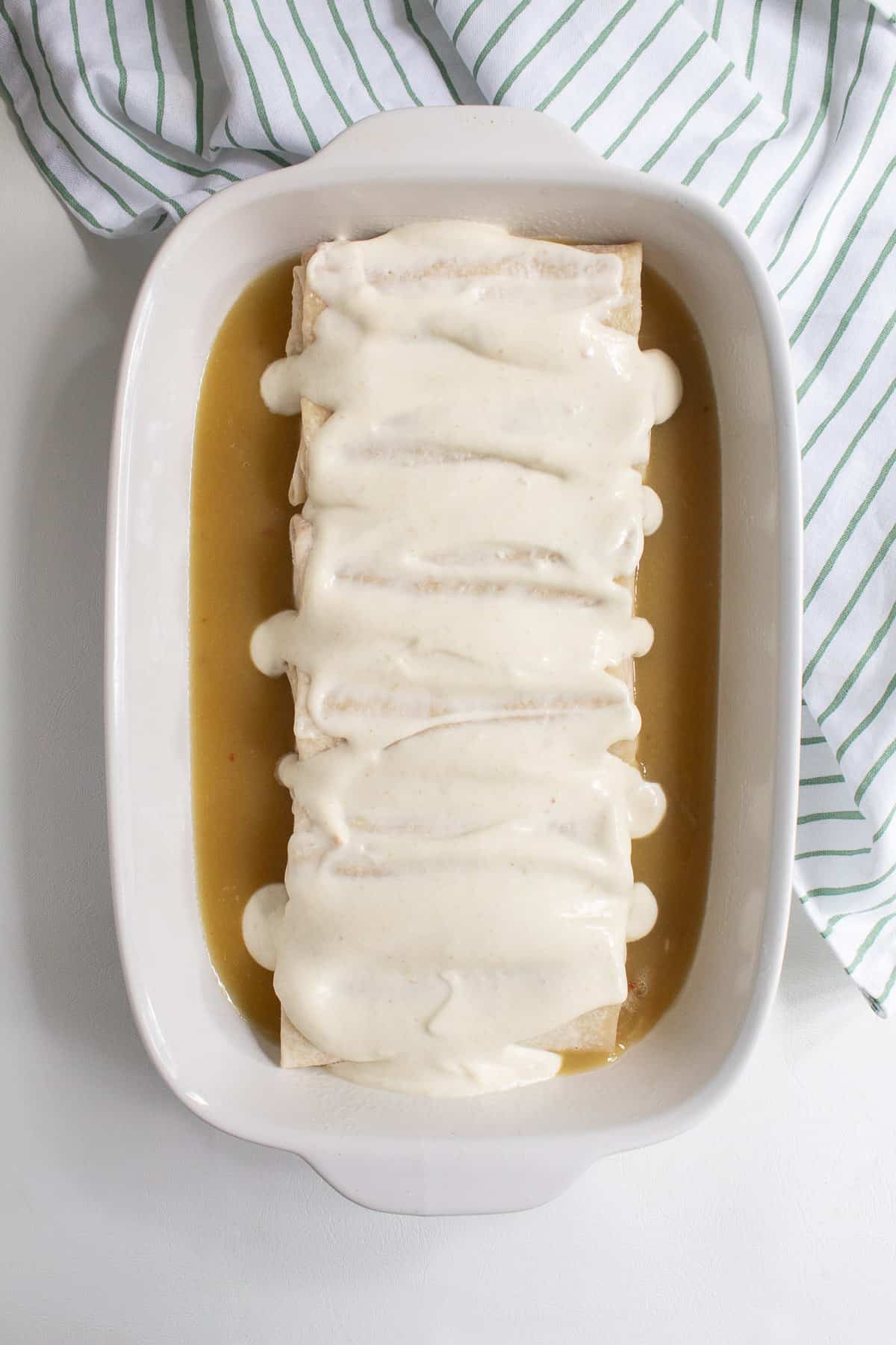 The sour cream and enchilada sauce mixture is spread over the burritos in the casserole dish.