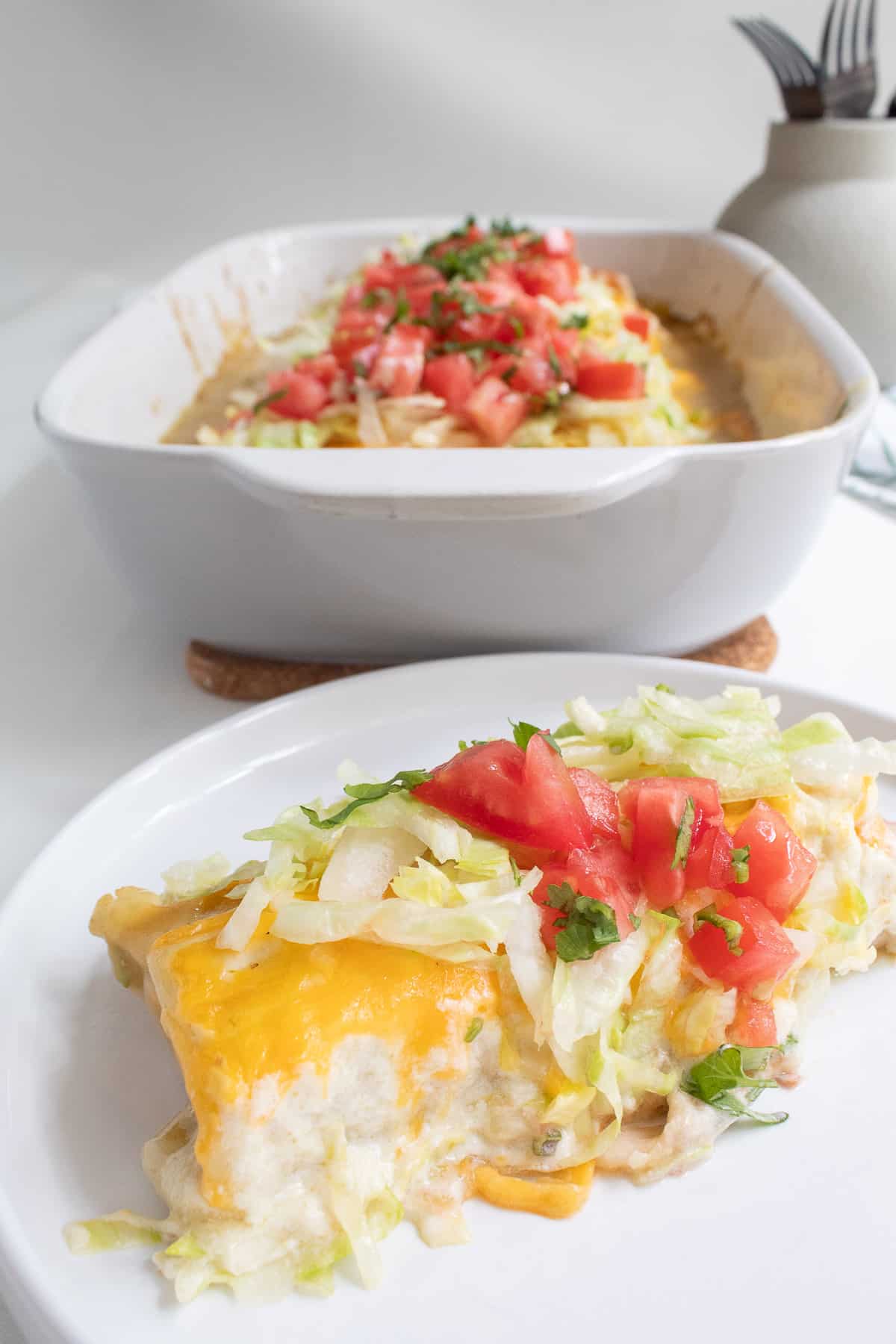 A single serving of the burrito casserole is on a white plate with the casserole dish in the background.