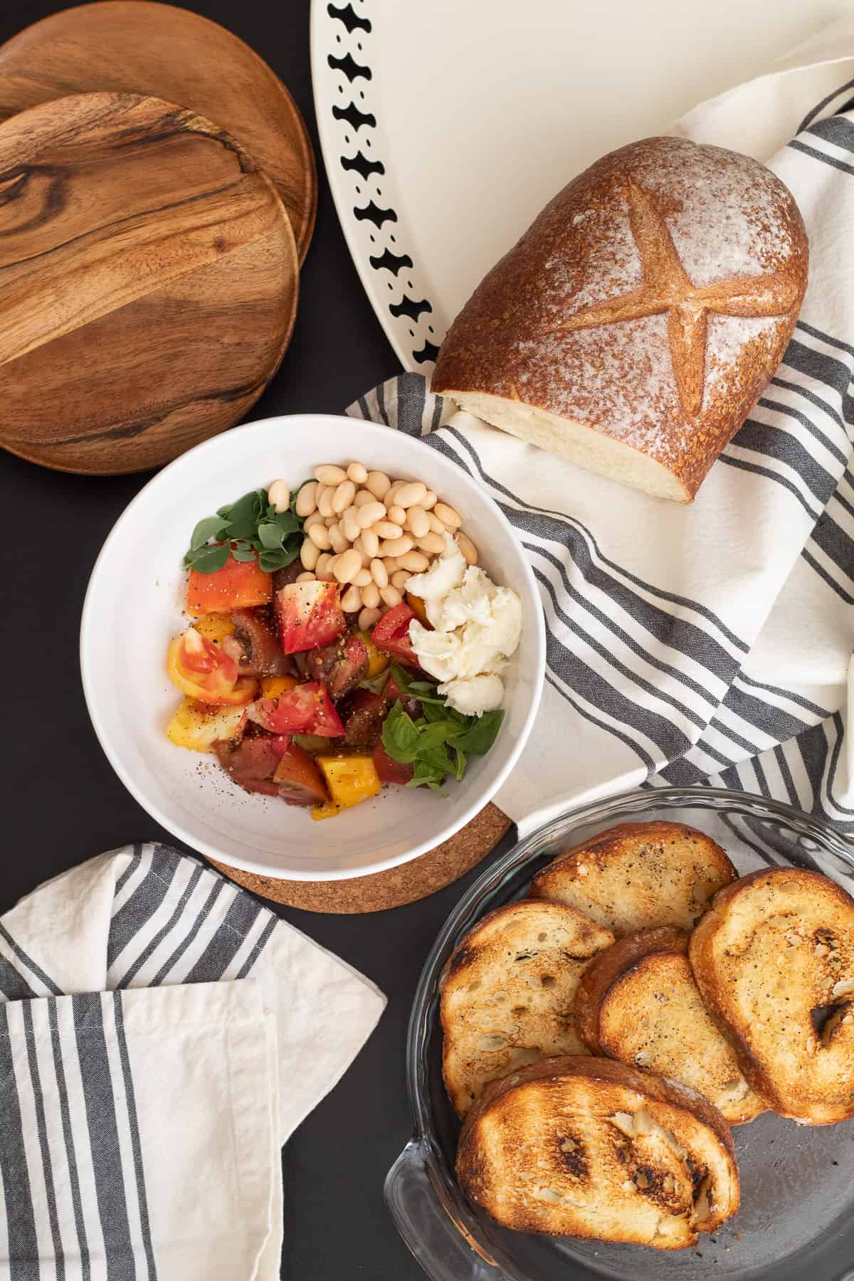 The grilled bread sits in a pie plate at the bottom of the image with the bowl of the rest of the salad ingredients in the center. Everything sits on a black surface with gray and white striped towels.