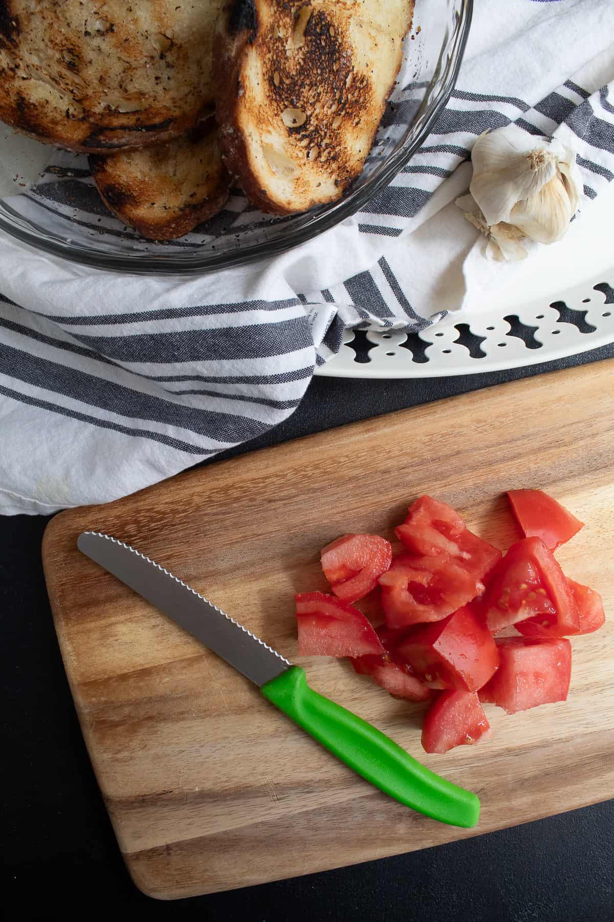 Tomatoes are roughly chopped on a wooden cutting board with a green-handled knife.