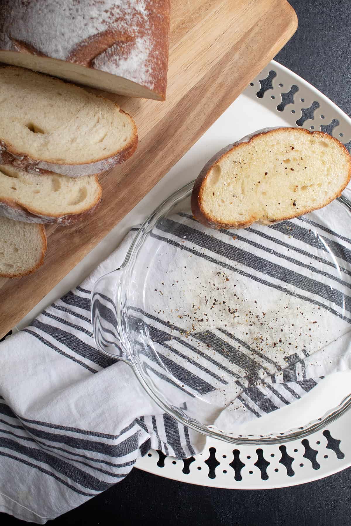 Sliced bread sits on the edge of a pie plate containing olive oil, salt, and pepper.