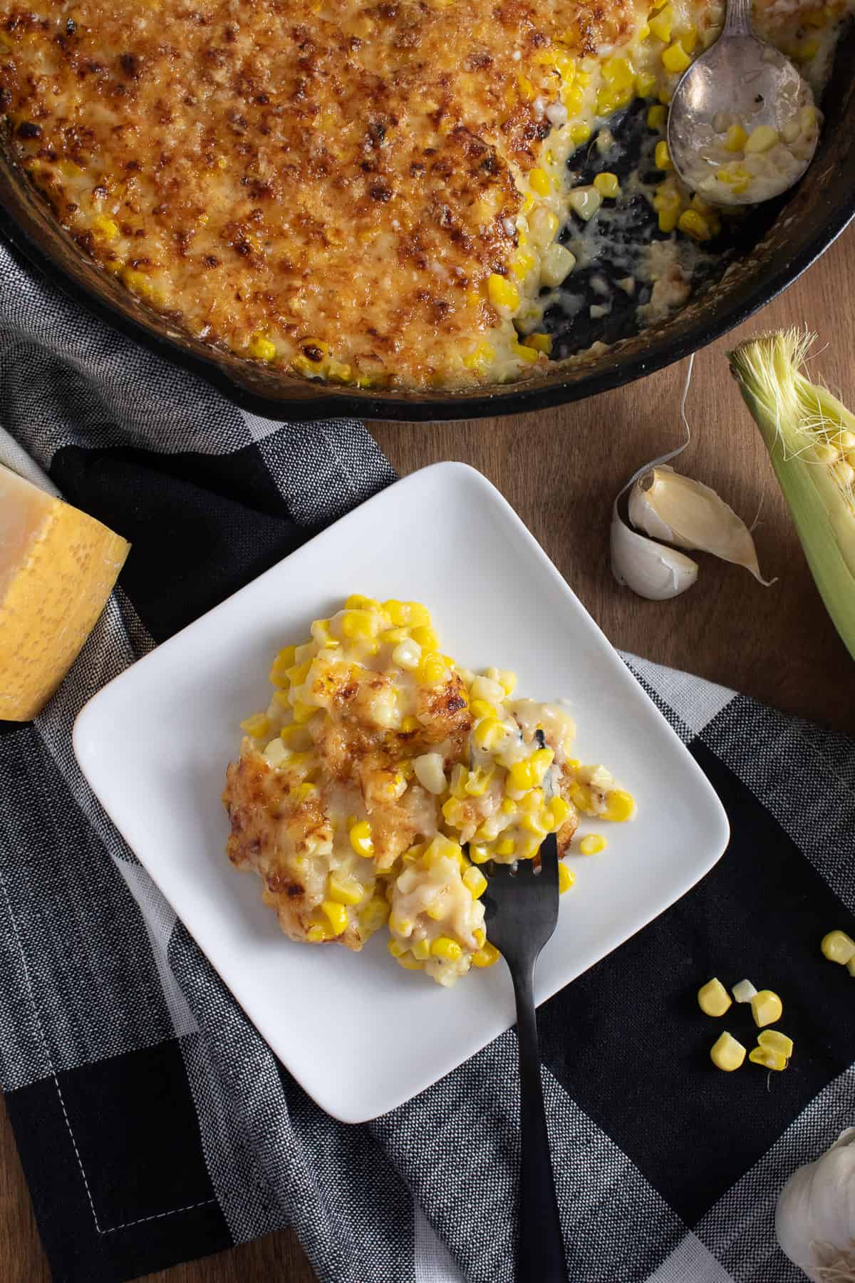 Detail of a serving of the gratin on a white square plate shows kernels of corn in a thick sauce.