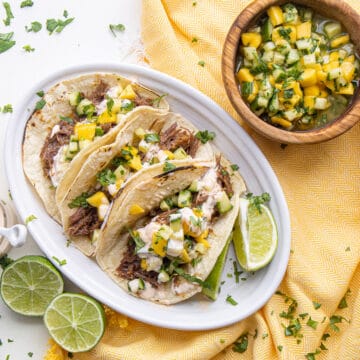 Plated tacos sit on a yellow napkin next to halved limes and a bowl of salad for topping the tacos.