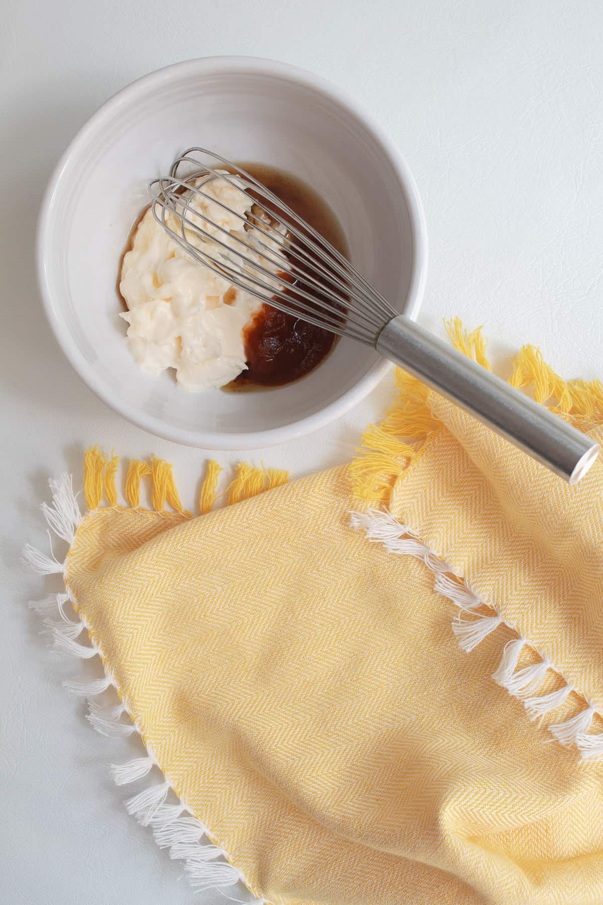 Mayonnaise, sriracha, and sesame oil are combined in a small white bowl using a wire whisk.