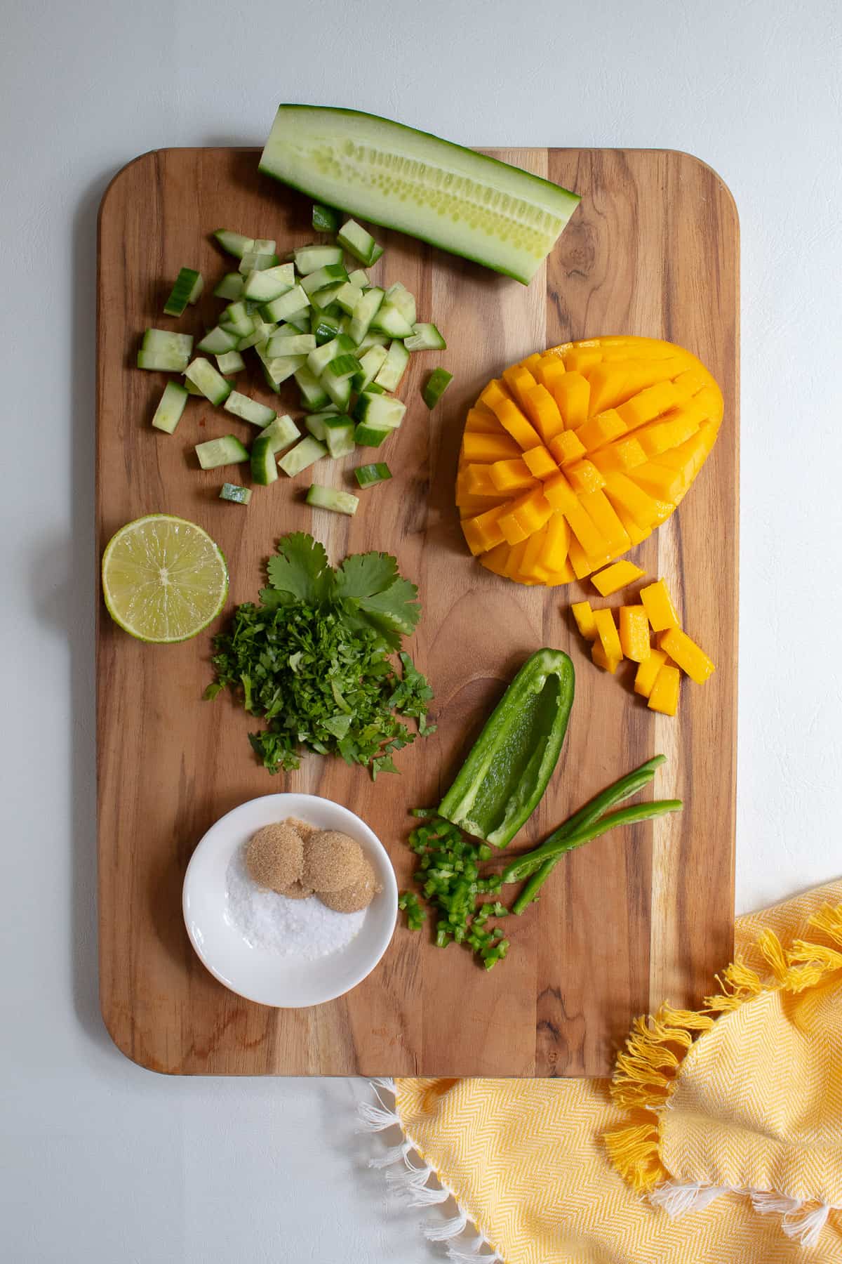 Ingredients for the mango cucumber salad are diced and arranged on a wooden cutting board.