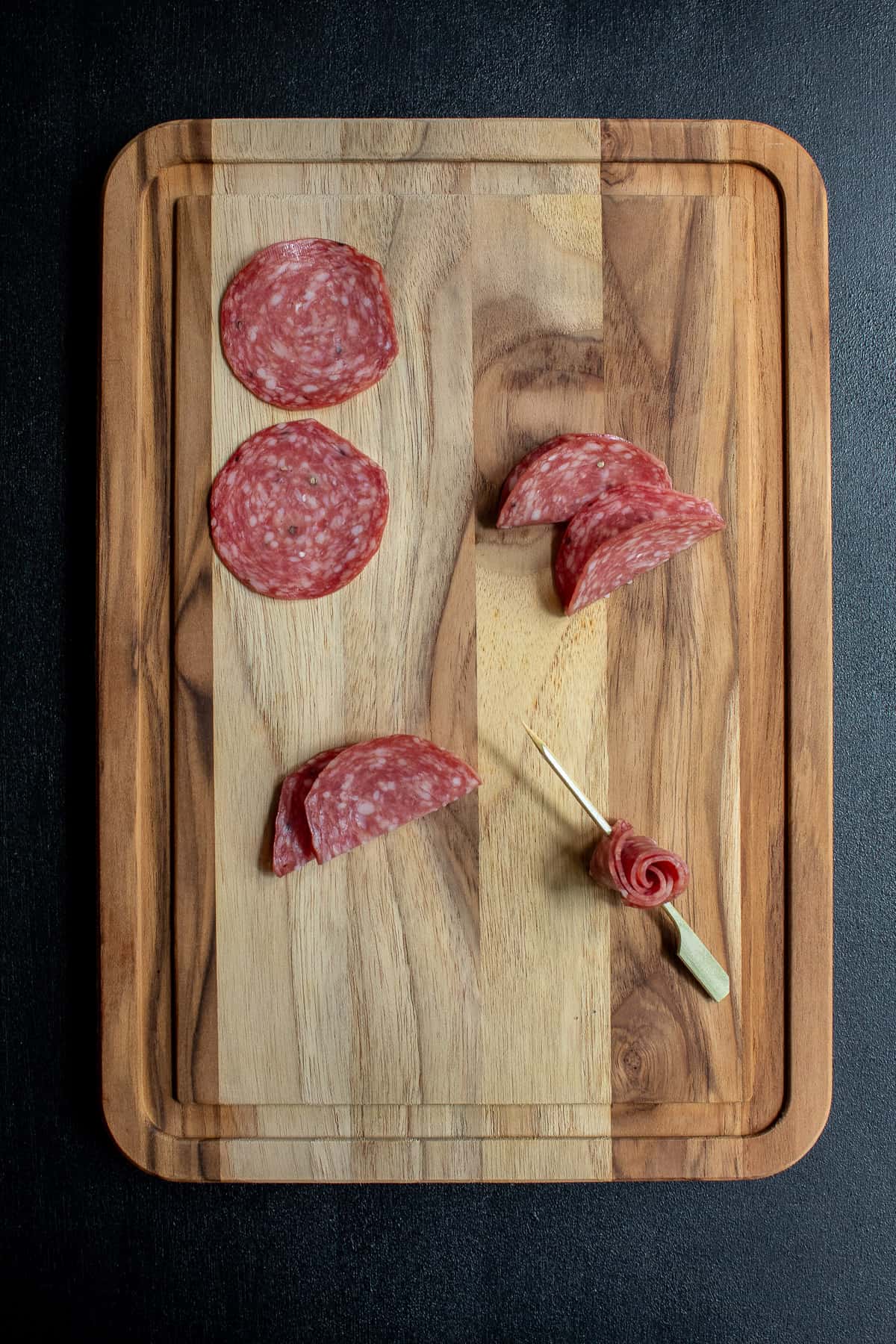 Steps for creating a salami rose on a skewer are illustrated on a wood cutting board.