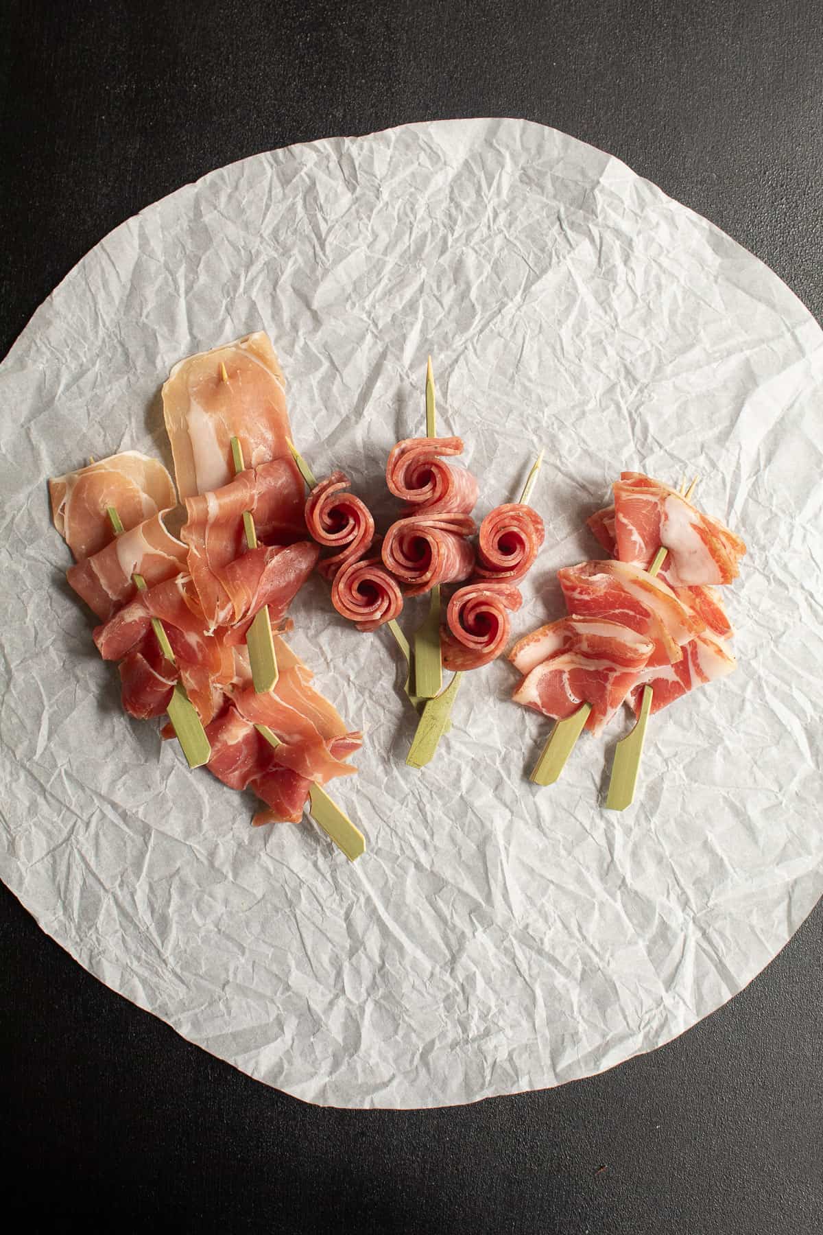 Prosciutto ribbons, salami roses, and coppa fans are displayed on a circle of wrinkled parchment.