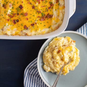 A serving of the loaded potatoes on a light blue plate sits next to a casserole dish of the mashed potatoes.