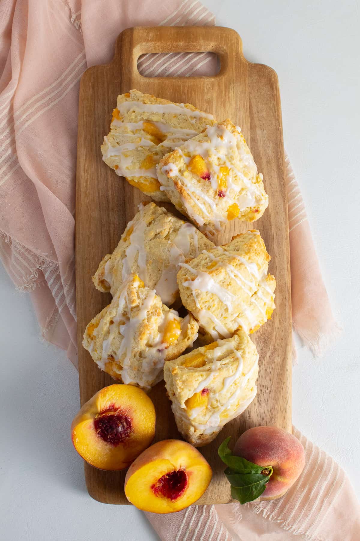 The biscuits are arranged on a rectangular wooden tray alongside fresh peach halves.