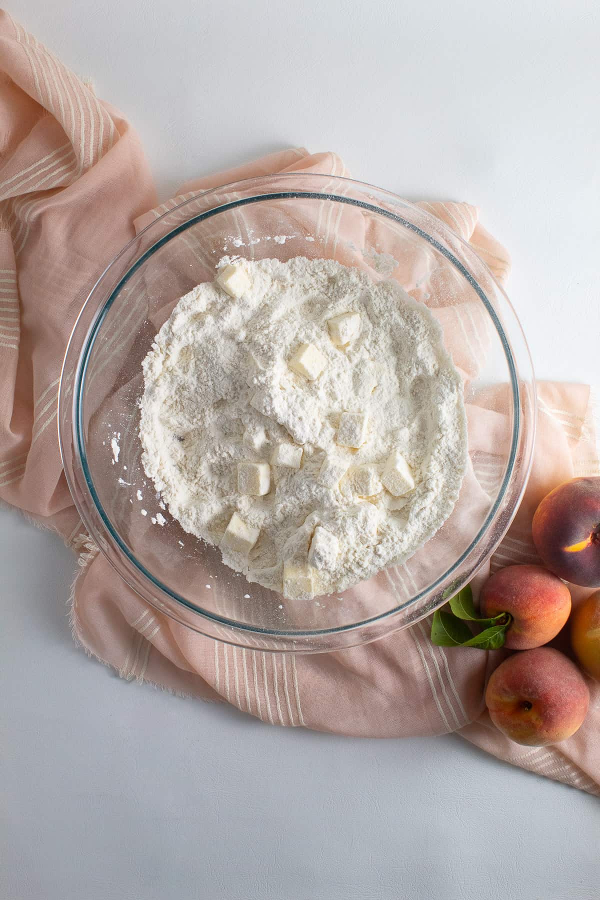 Chunks of diced butter are tossed with the dry ingredients in the bottom of the clear glass bowl.