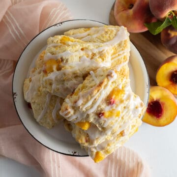 The glazed biscuits are piled on a black and white plate over a peach cloth-draped surface.