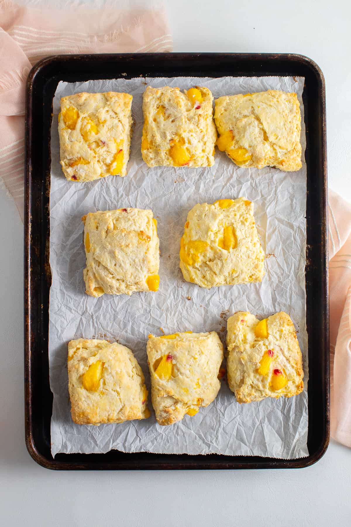 The baked biscuits sit on the parchment-lined pan and have puffed up with golden edges.