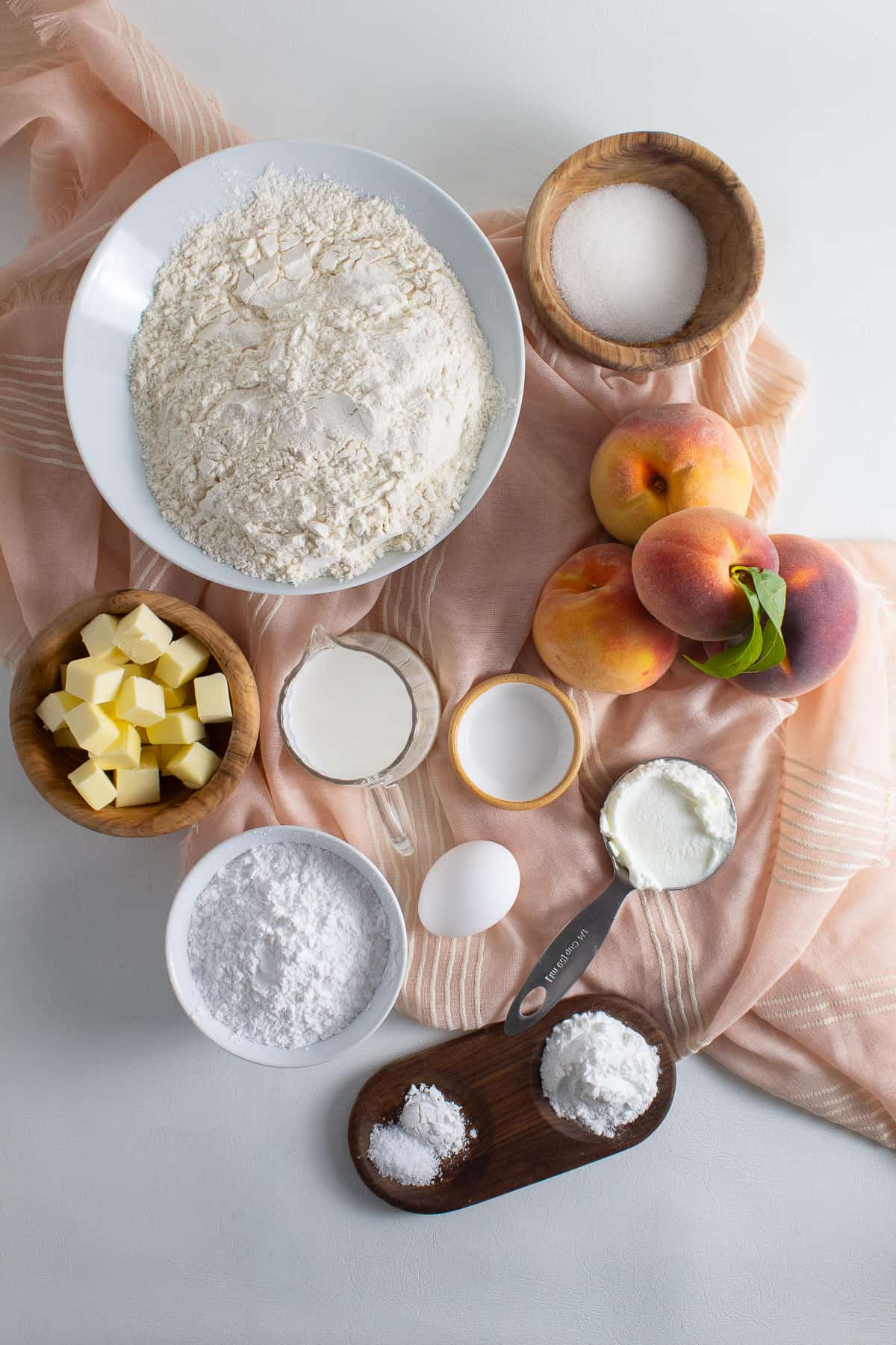 Ingredients for the peach biscuits are displayed on a white surface draped with a peach colored cloth.