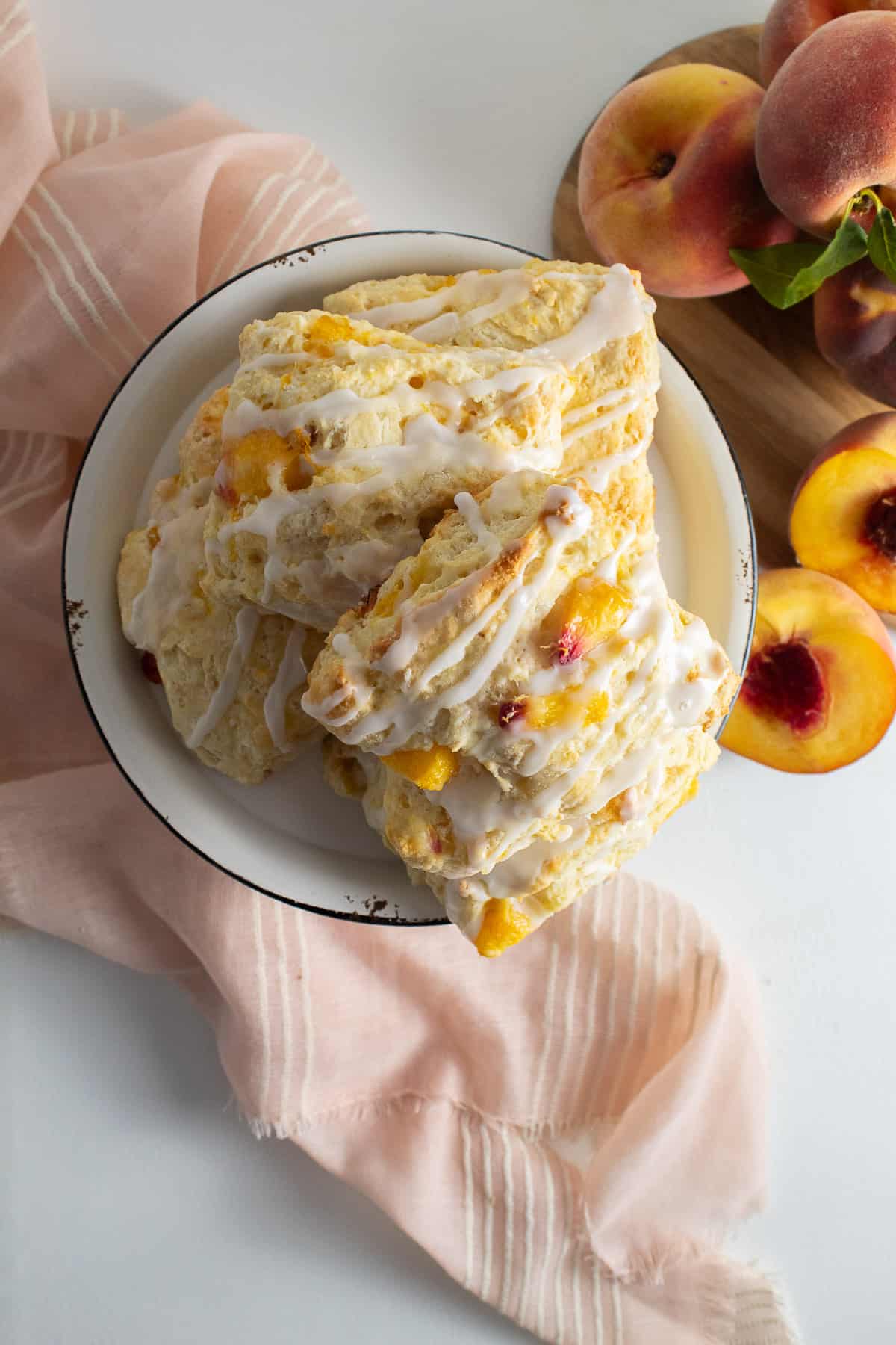 Biscuits are piled high in the center of the image, with a peach cloth and fresh peaches in the background.