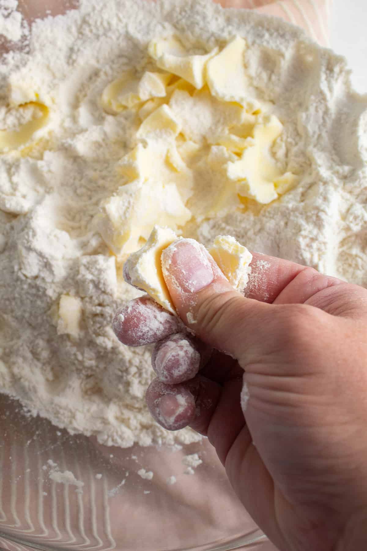 Butter is pressed between the thumb and fingers, creating a flat disc that is coated with flour.