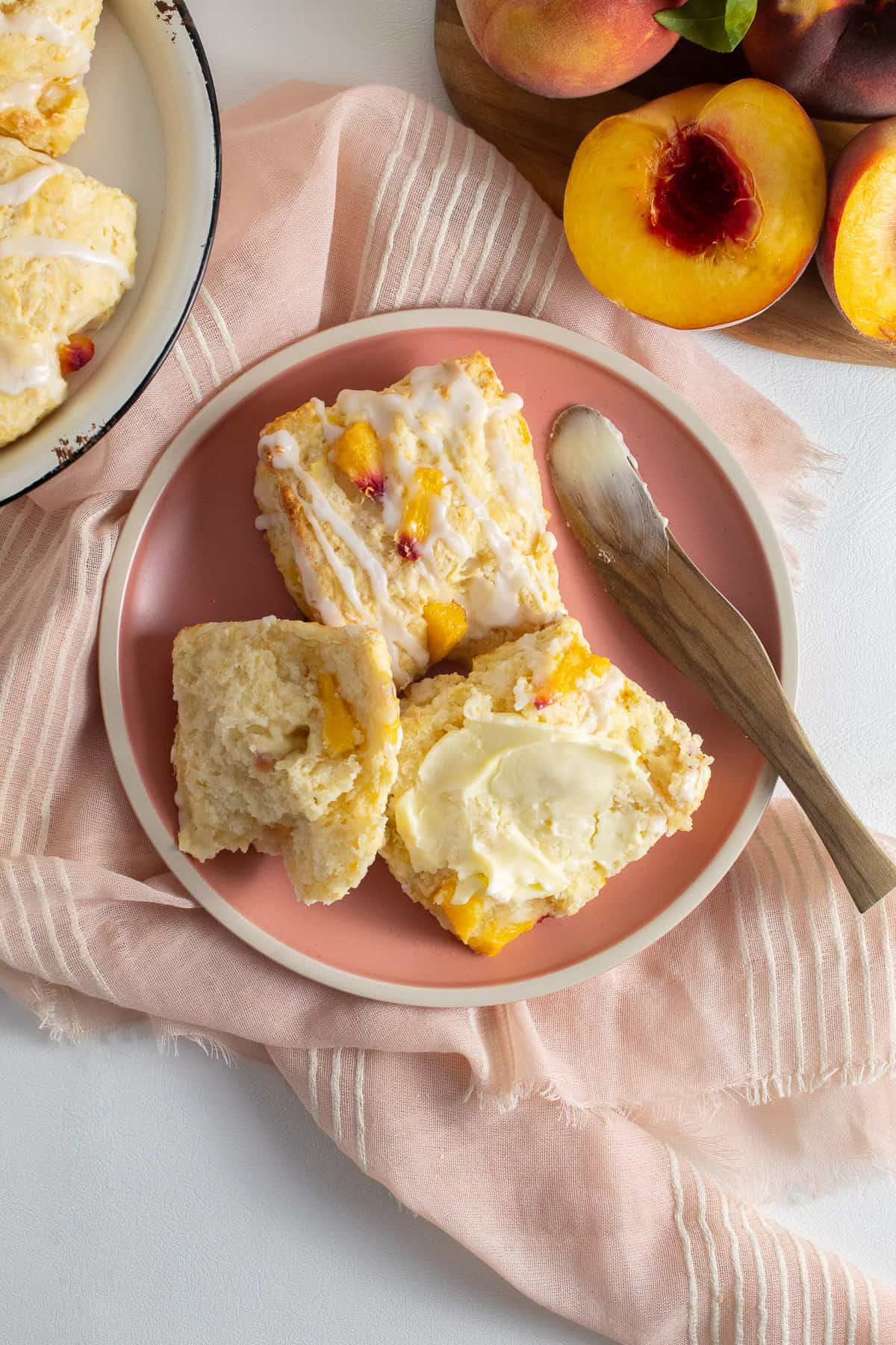 A split biscuit sits on a pink plate and is spread with butter.