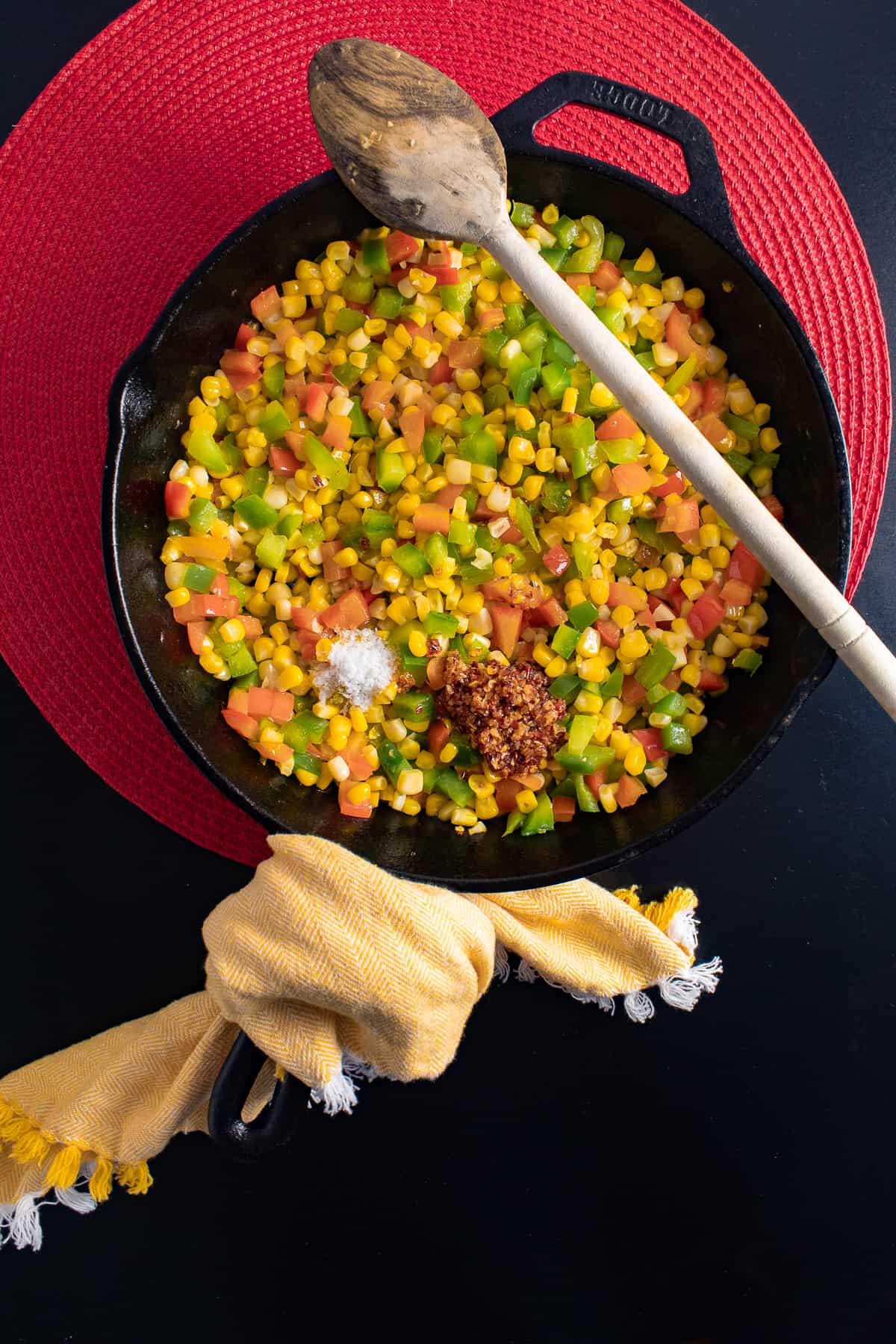 Chili onion crunch and salt are added to the skillet with the corn and peppers.