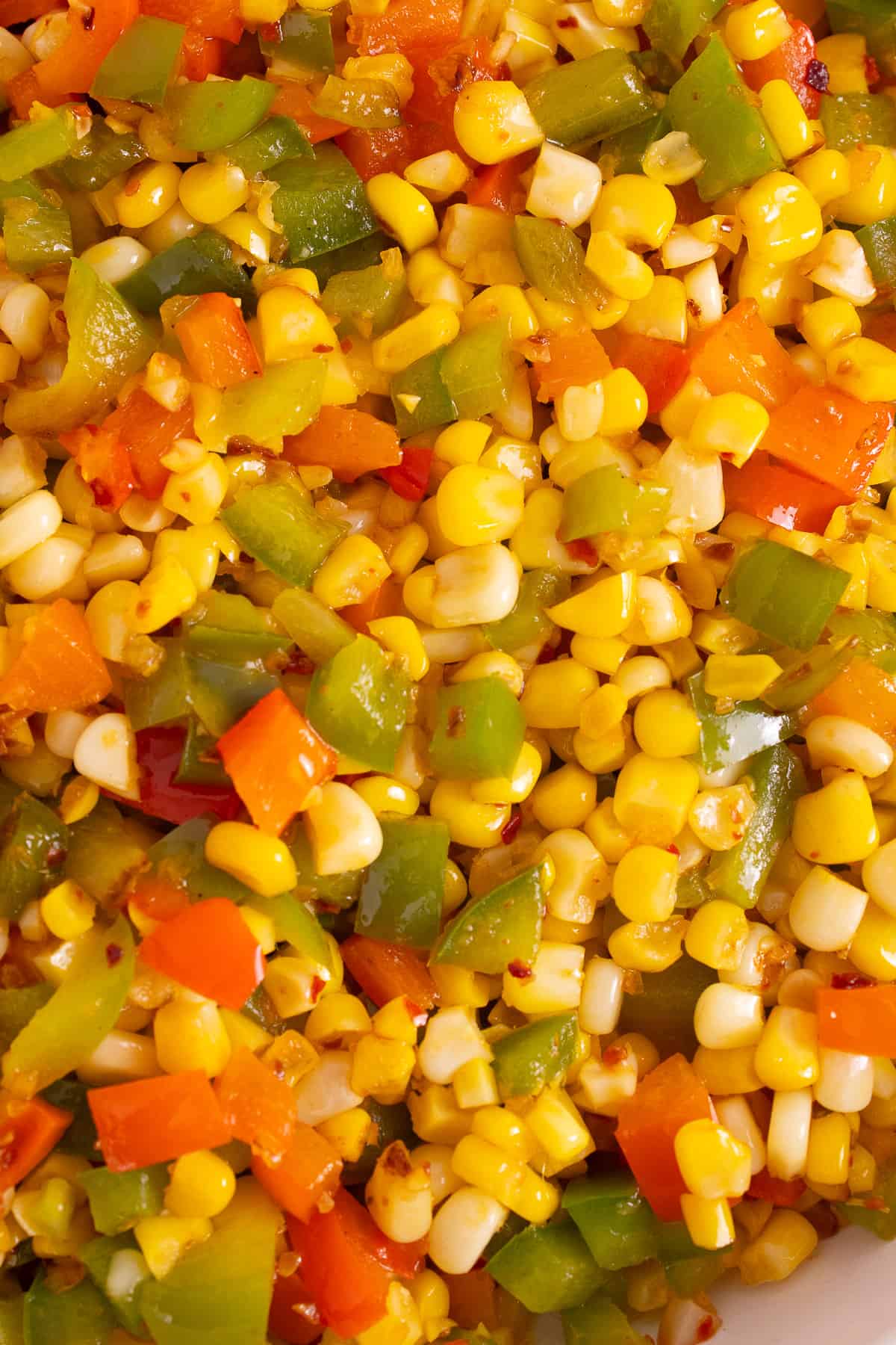 A close-up detail image of the side dish with a mixture of yellow, green, and red vegetables flecked with chili pieces.