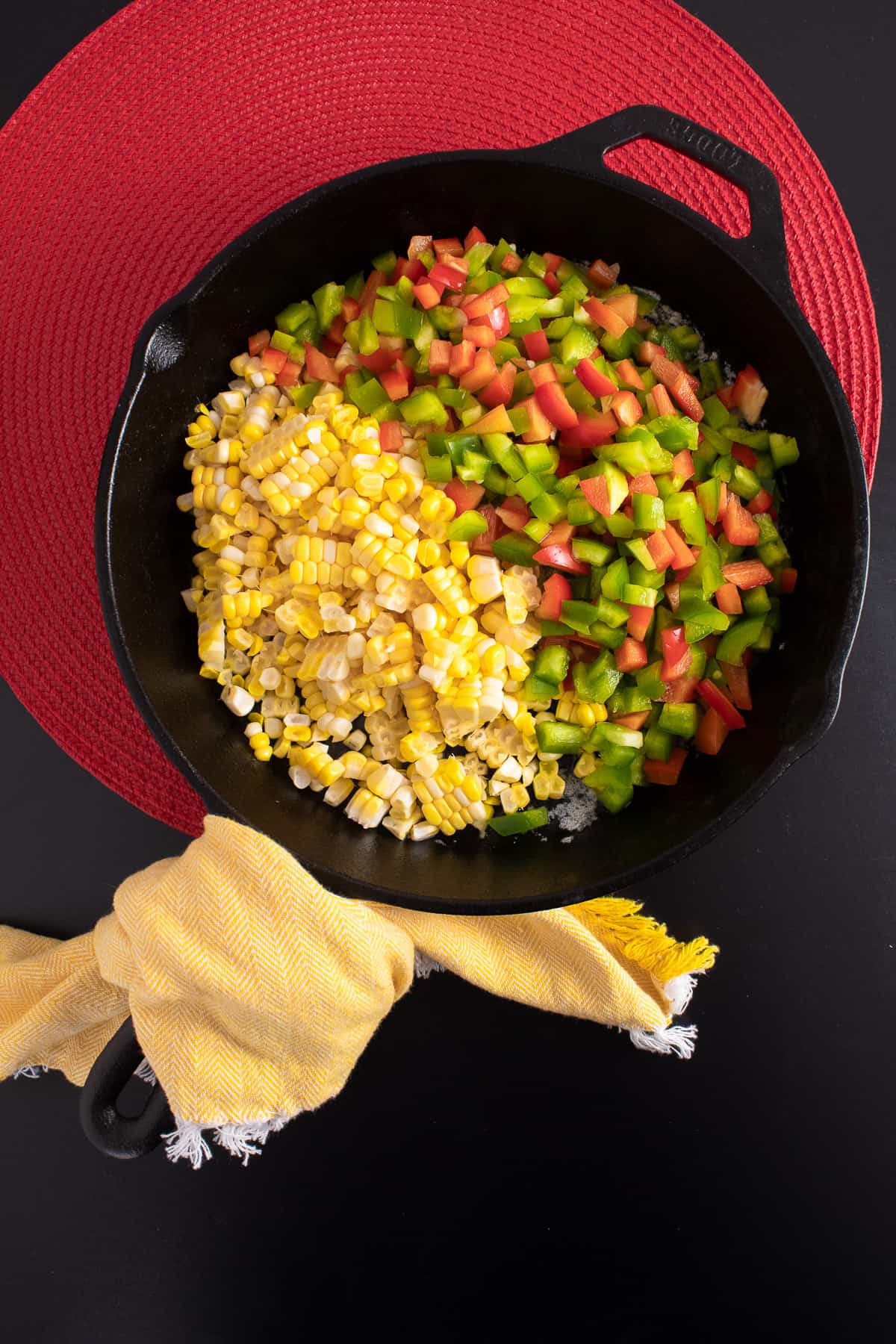 Diced red and green peppers and corn kernels are added to the cast iron skillet.