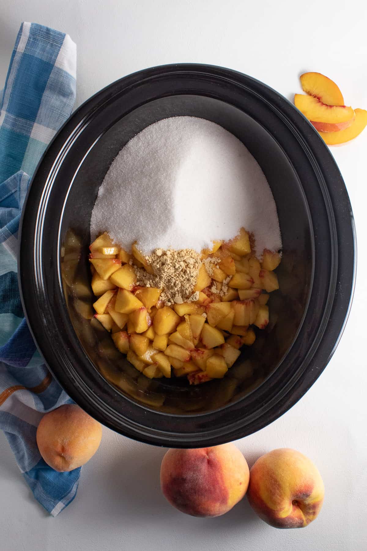 The diced peaches, sugar, and ground ginger are piled into a large crock.