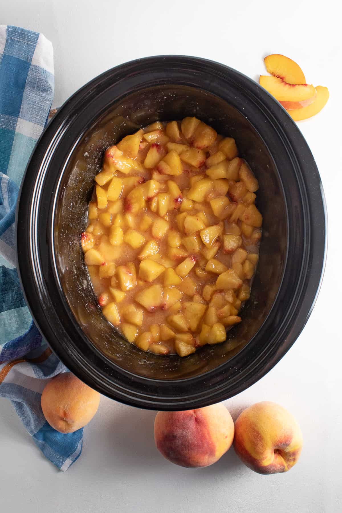 The peaches and sugar are stirred together in the crock and the mixture looks thick and syrupy.