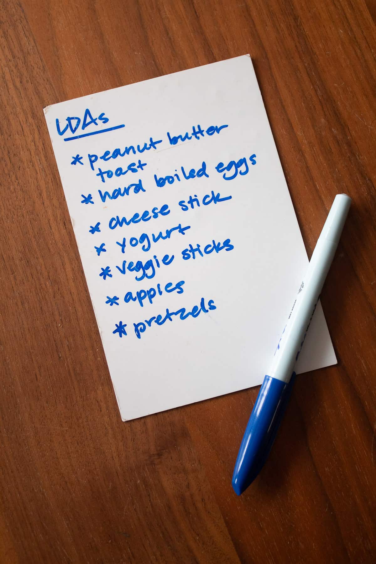 A list of foods titled "LDAs" on a white pad with a blue pen placed on top.