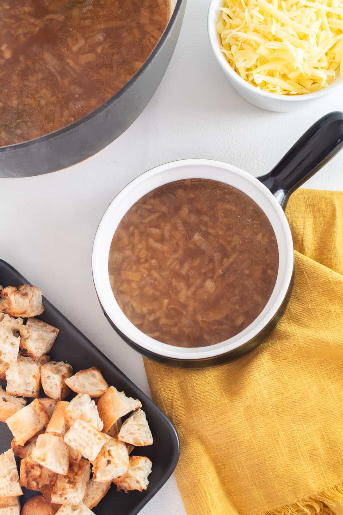 A serving of soup in a handled bowl with croutons and shredded cheese in containers nearby.