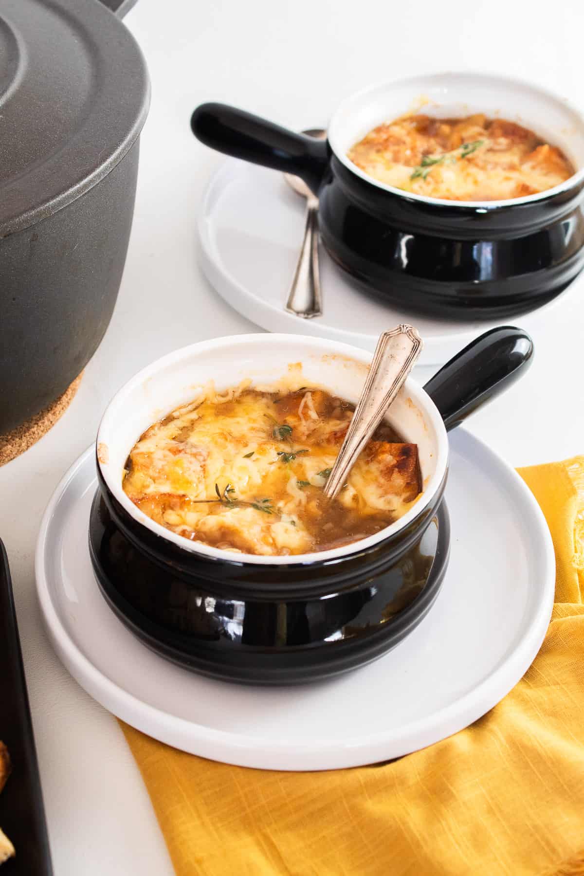 Two black handled bowls are filled with soup, croutons, and cheese and topped with thyme sprigs.