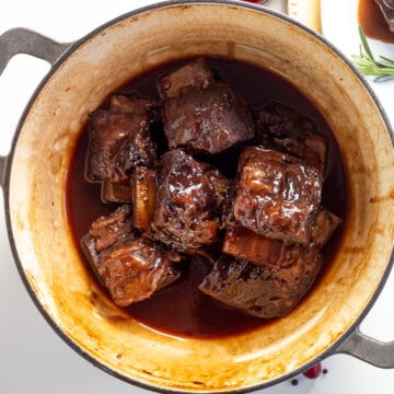 Prepared short ribs are bathed in a glossy sauce in the bottom of a large pot.