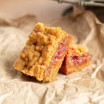 Two cookie bars are resting on a crumpled brown paper and the red jelly filling is visible.