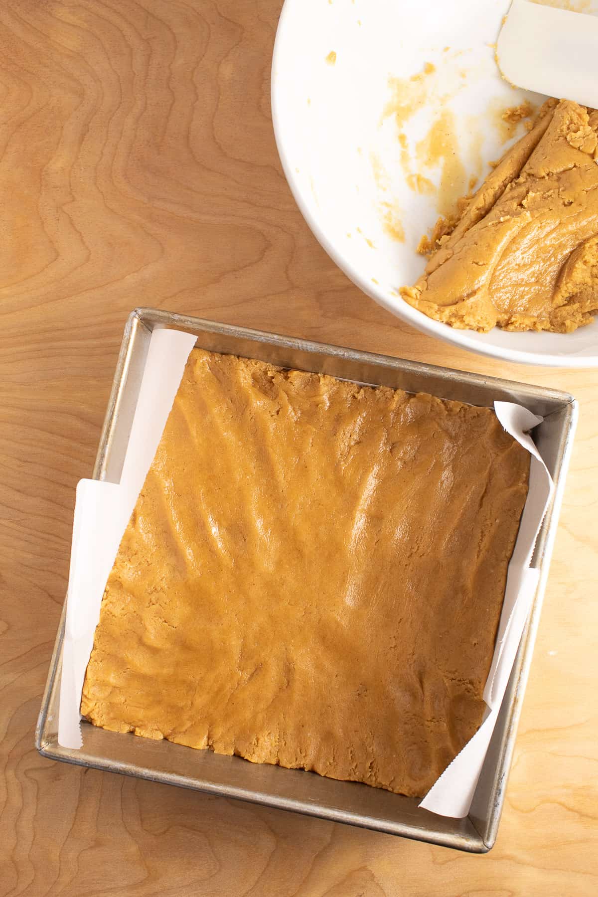 Half of the dough is pressed into the bottom of a square pan lined with parchment paper.