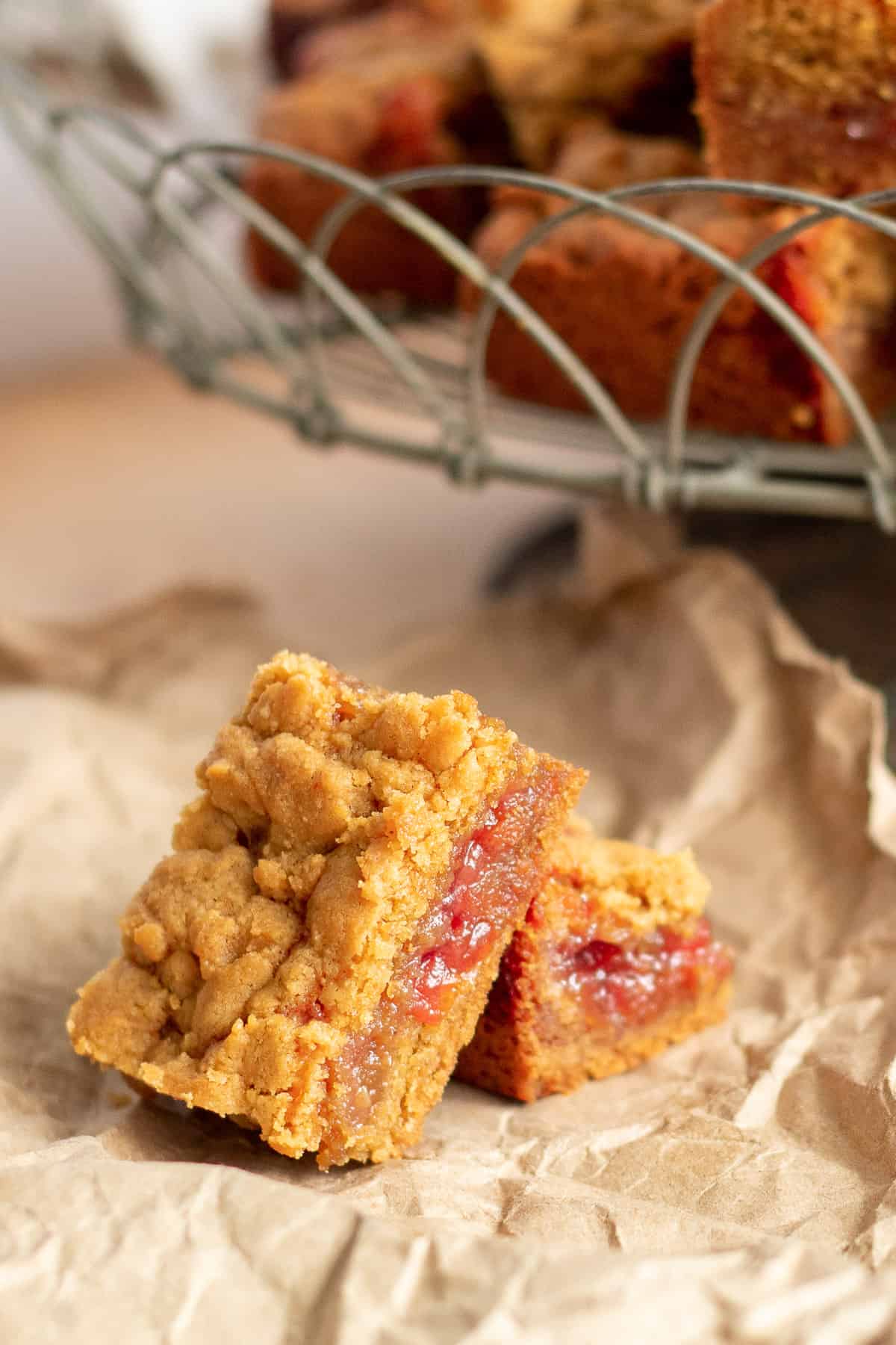 Two cookie bars are resting on a crumpled brown paper with a basket of more bars in the background.