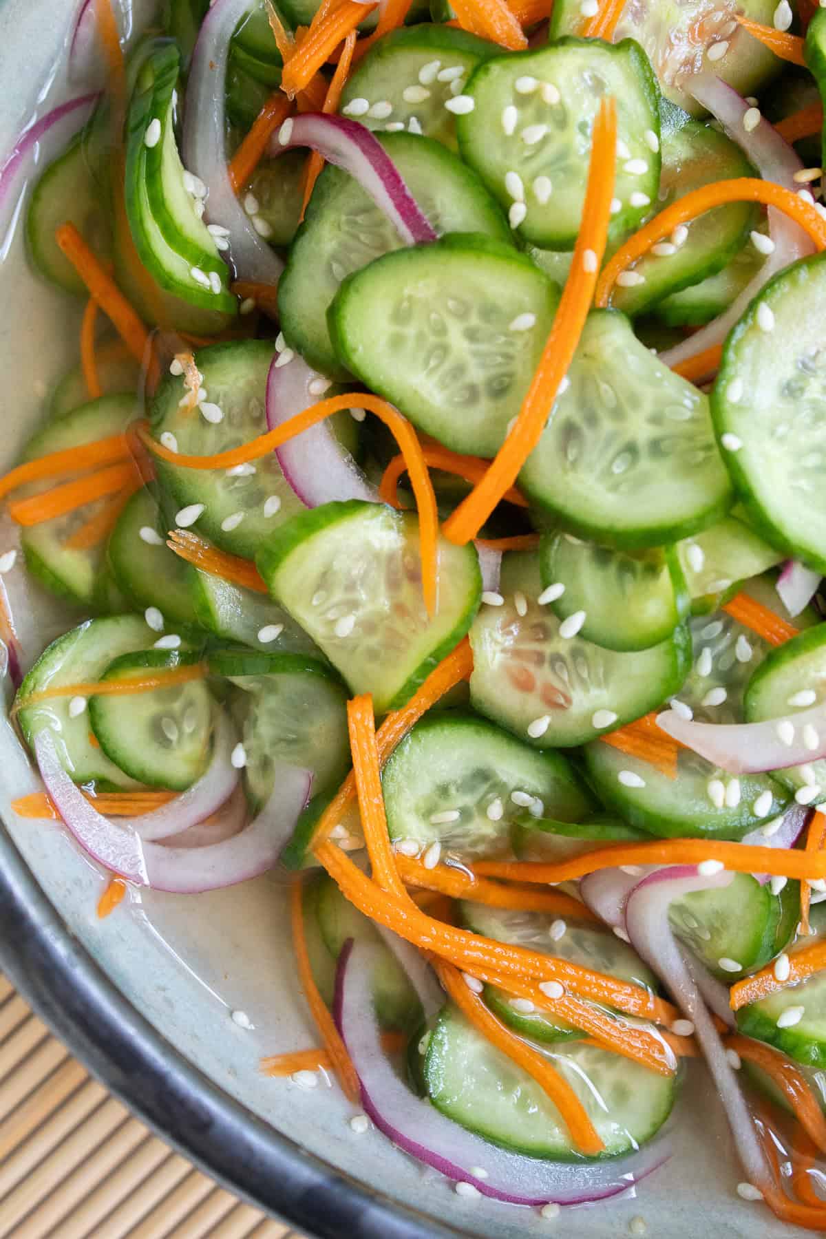 A detail image of the cucumber salad, with thinly sliced carrots, cucumber discs, red onion, and sesame seeds.