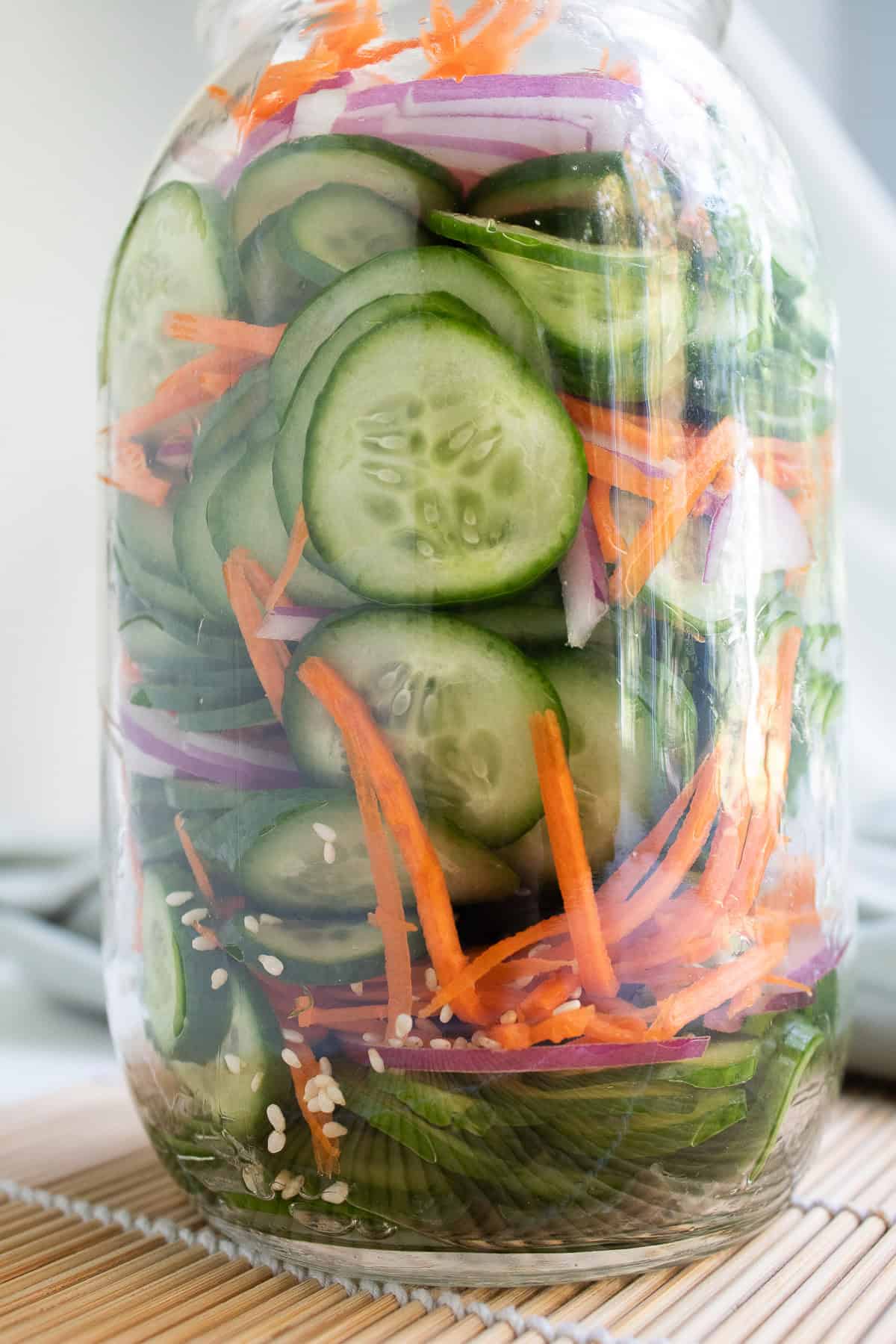 A quart jar is packed with layers of cucumber, red onion, carrot, and sesame seeds.