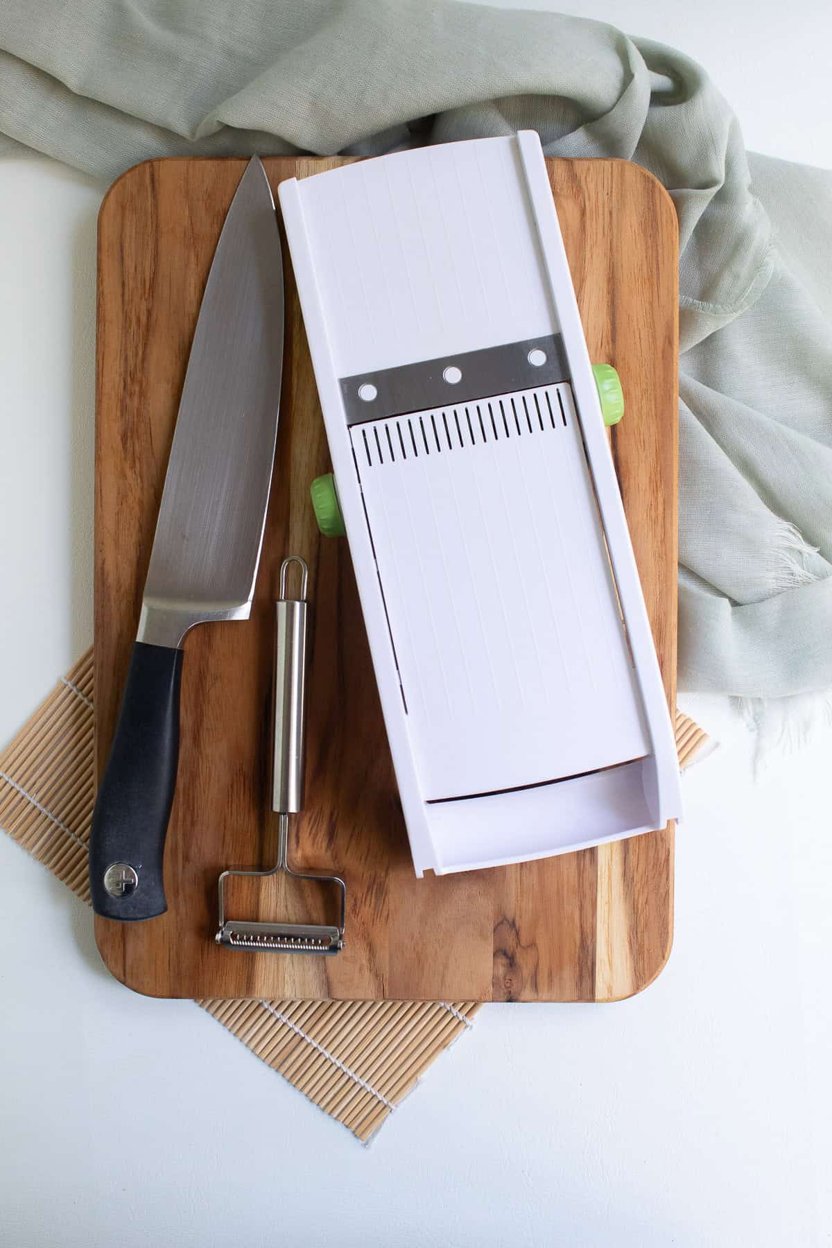 A chef's knife, julienne peeler, and a mandoline sit on a cutting board.