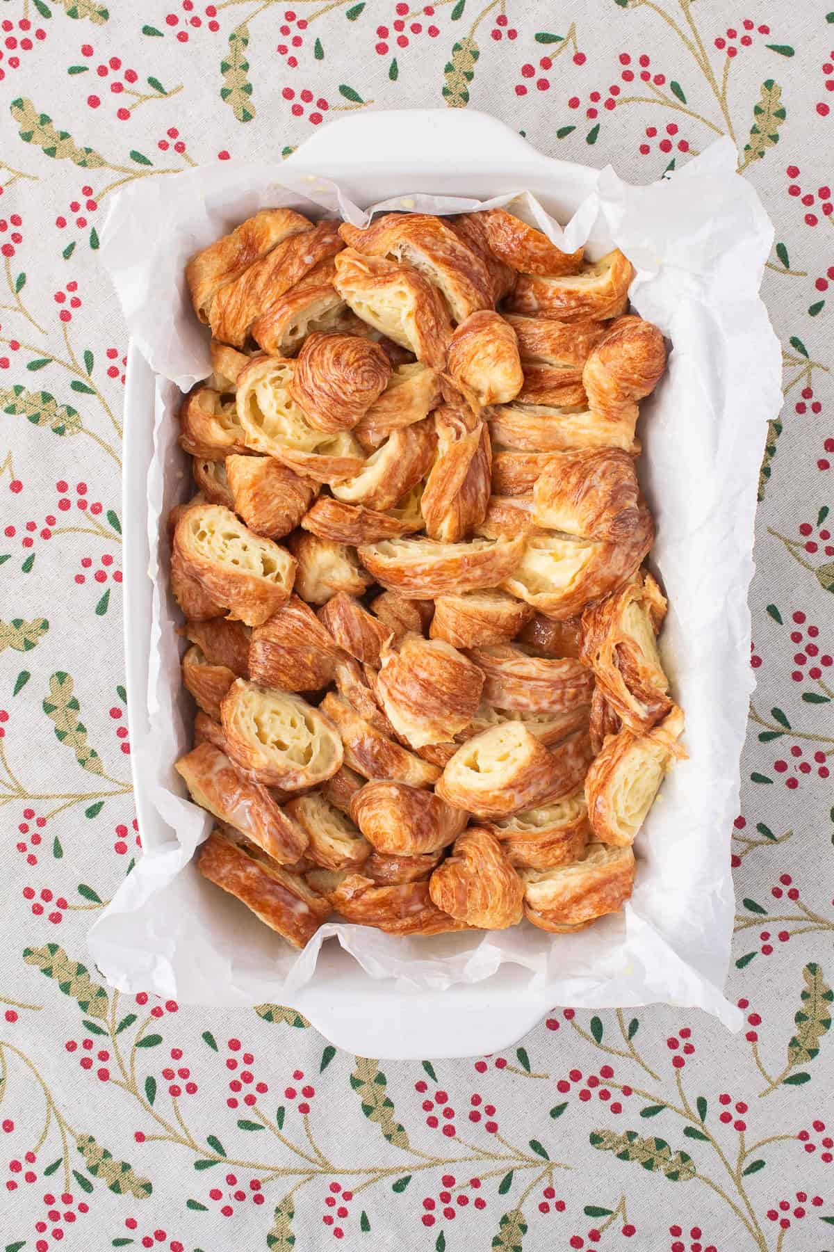 The croissants soaked in eggnog custard are transferred to a parchment-lined baking dish.