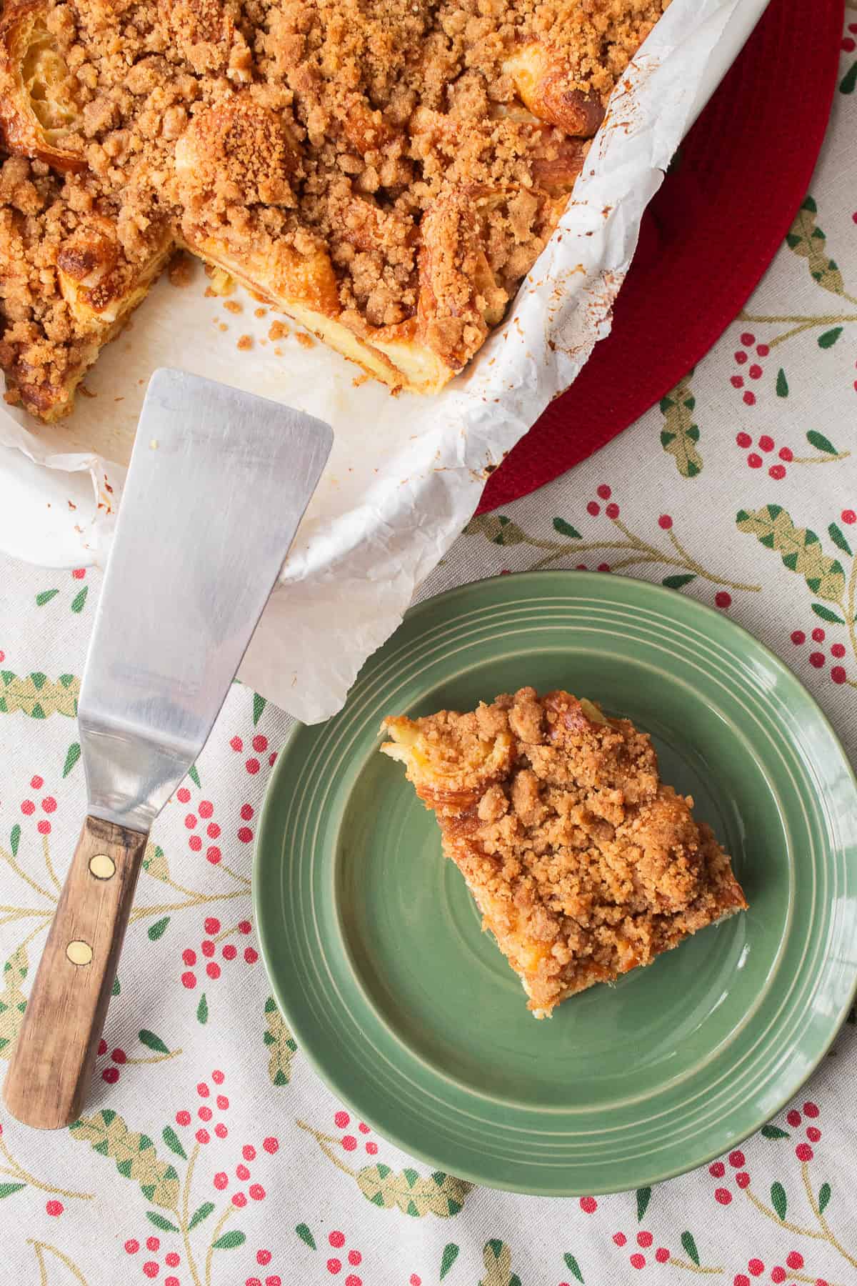 A slice of bread pudding is served from the baking dish on to a green plate.
