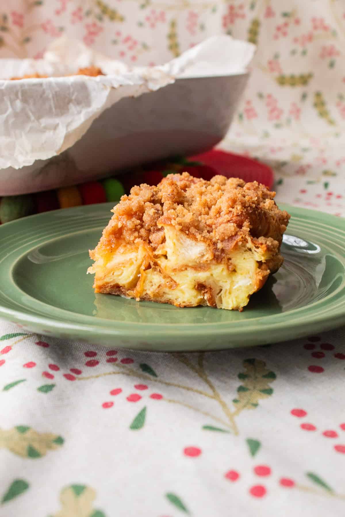 A slice of the baked bread pudding is on a green plate and the marbled texture and crumble topping are shown.