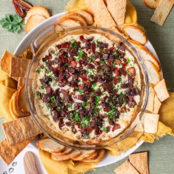 The baked dip is sprinkled with parsley, has golden edges, and is displayed on a round platter with crackers and chips around the sides.