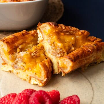 A baked croissant is sliced in half to reveal the tender filling of eggs, cheese, and sausage and a crisp and flaky exterior.