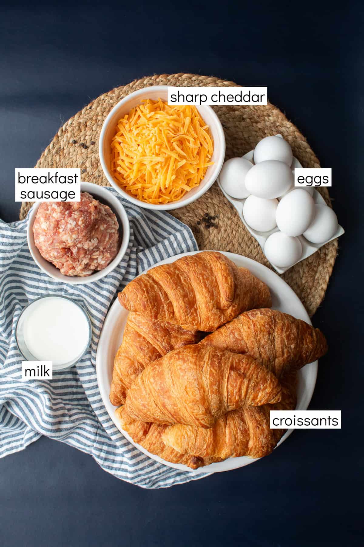 Ingredients for the recipe are displayed on a dark blue background and include white text labels: sharp cheddar, eggs, croissants, milk, and breakfast sausage.