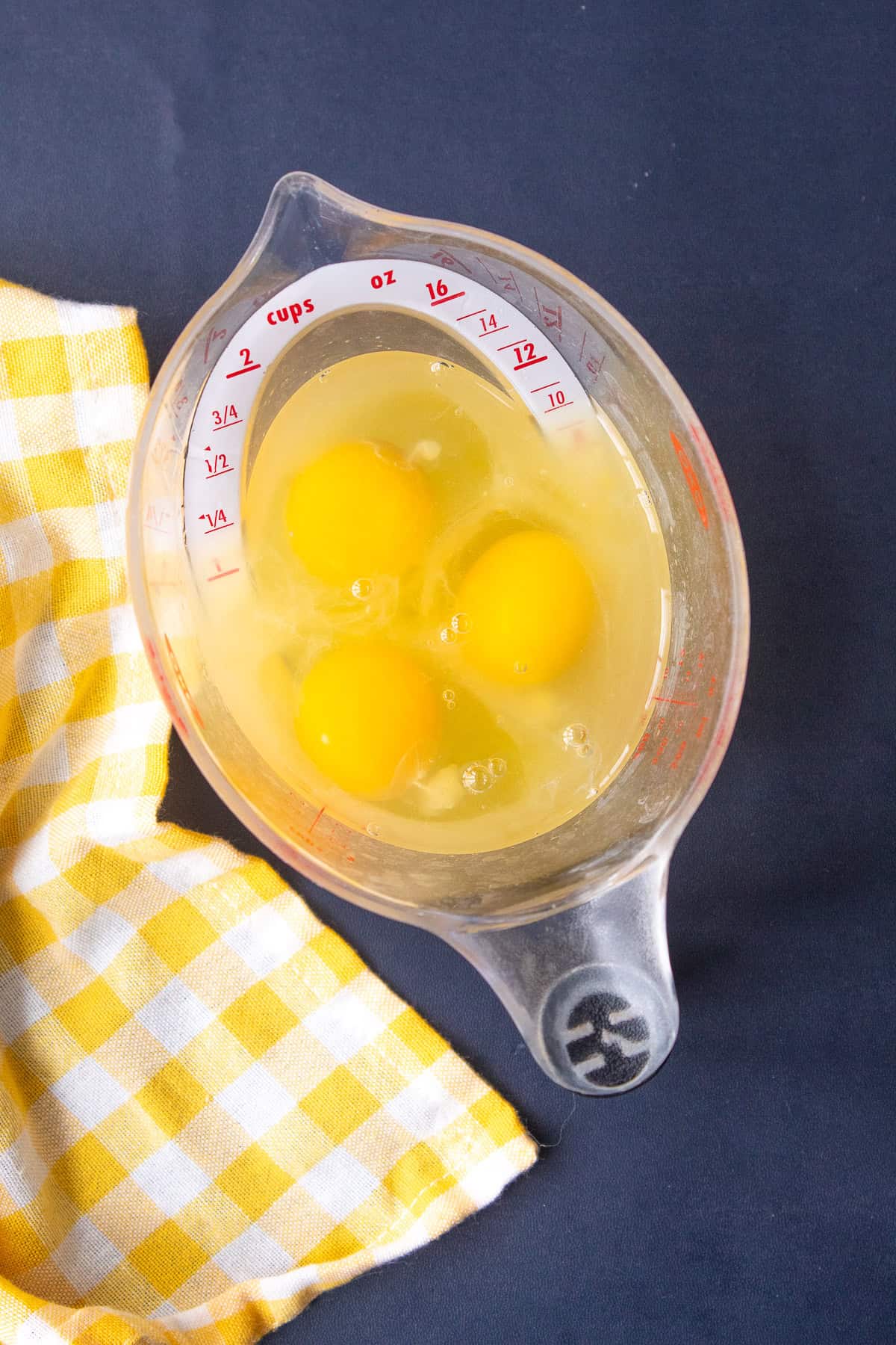 Whole eggs and lemon juice are added to a large measuring cup with a spout.