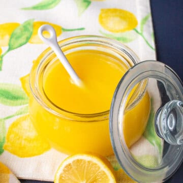 The bright yellow lemon curd is displayed in a glass jar with a white spoon.
