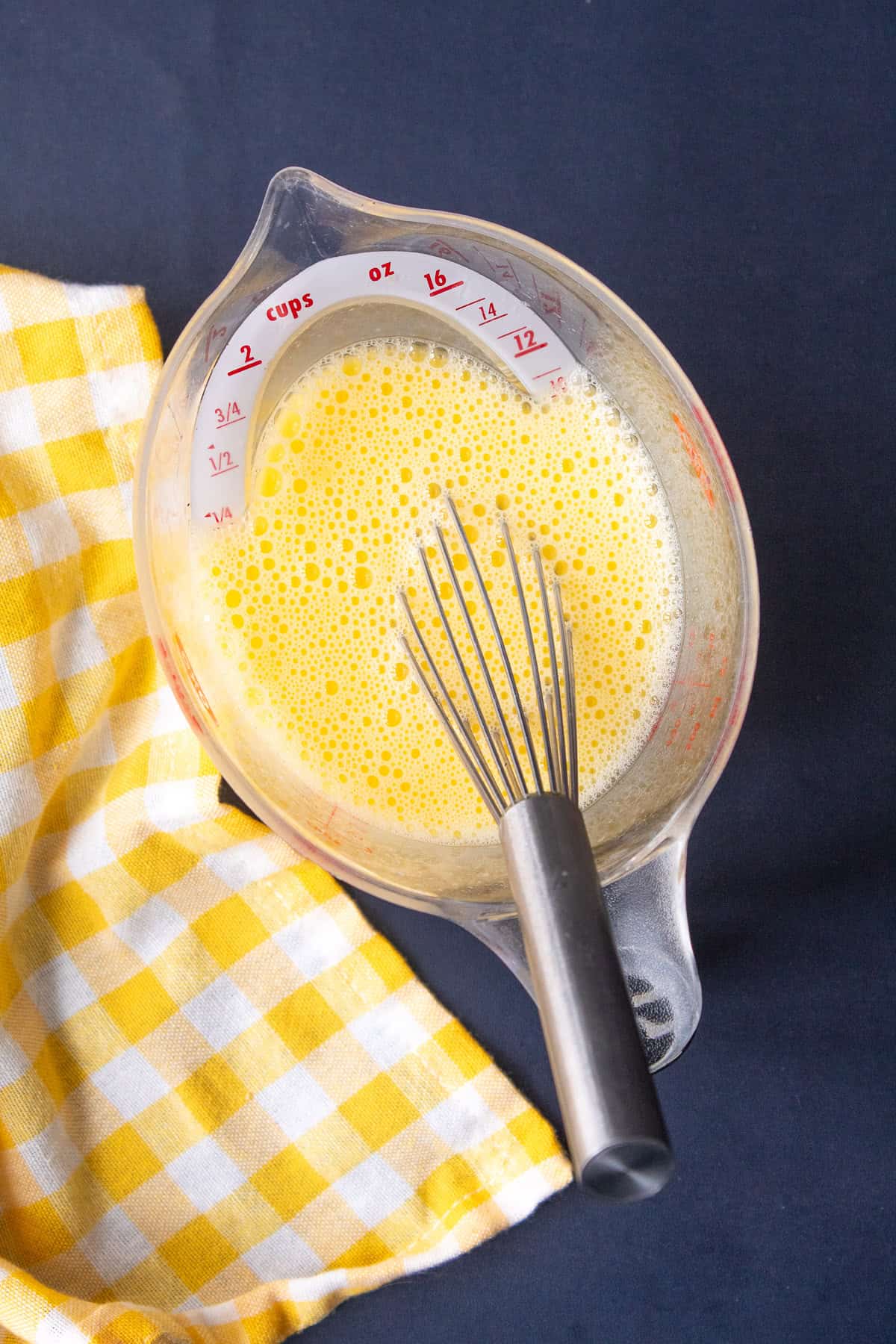 Eggs and lemon juice are vigorously whisked in a measuring cup with a spout until foamy and pale yellow.