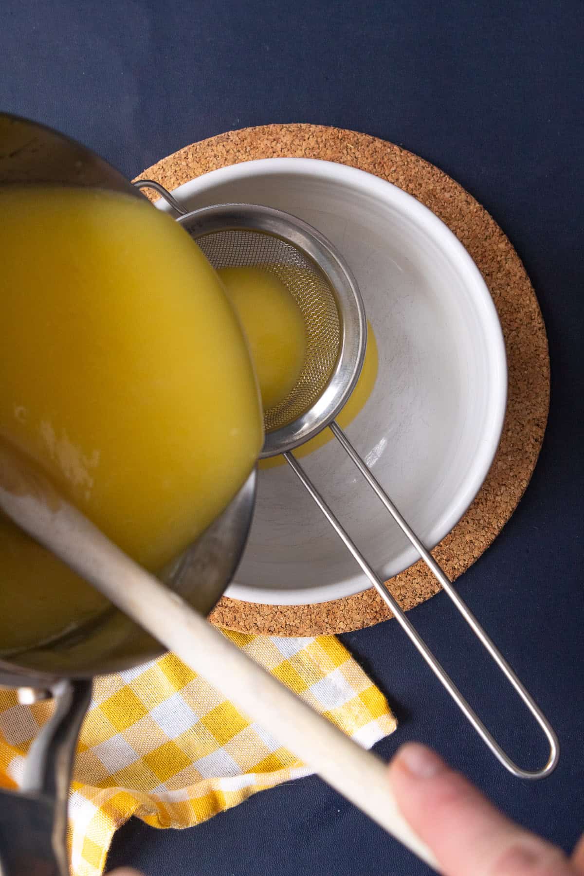 The cooked lemon curd is strained through a wire mesh strainer.
