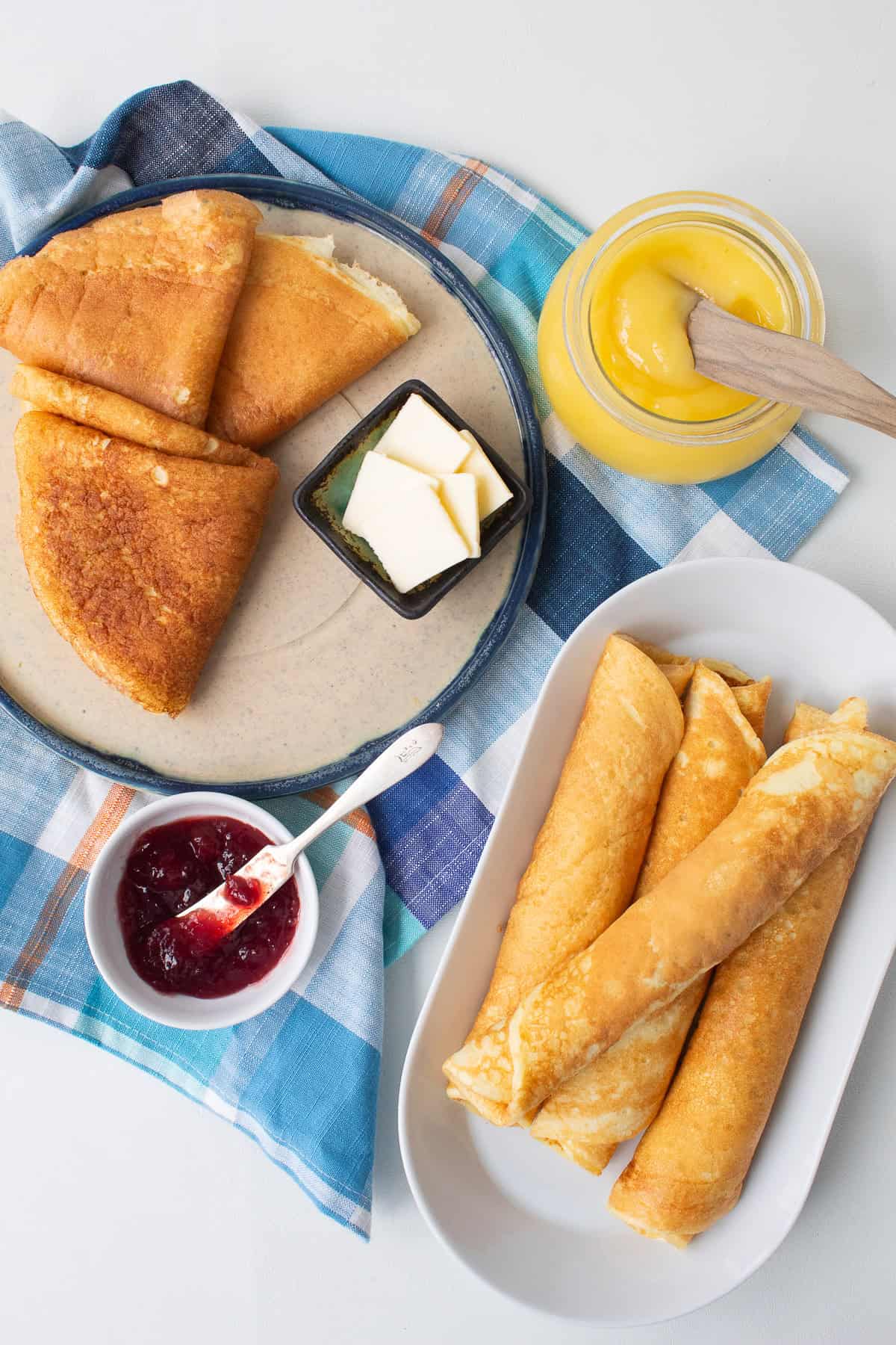 The pancakes are on various plates along with cherry jam, lemon curd, and butter.