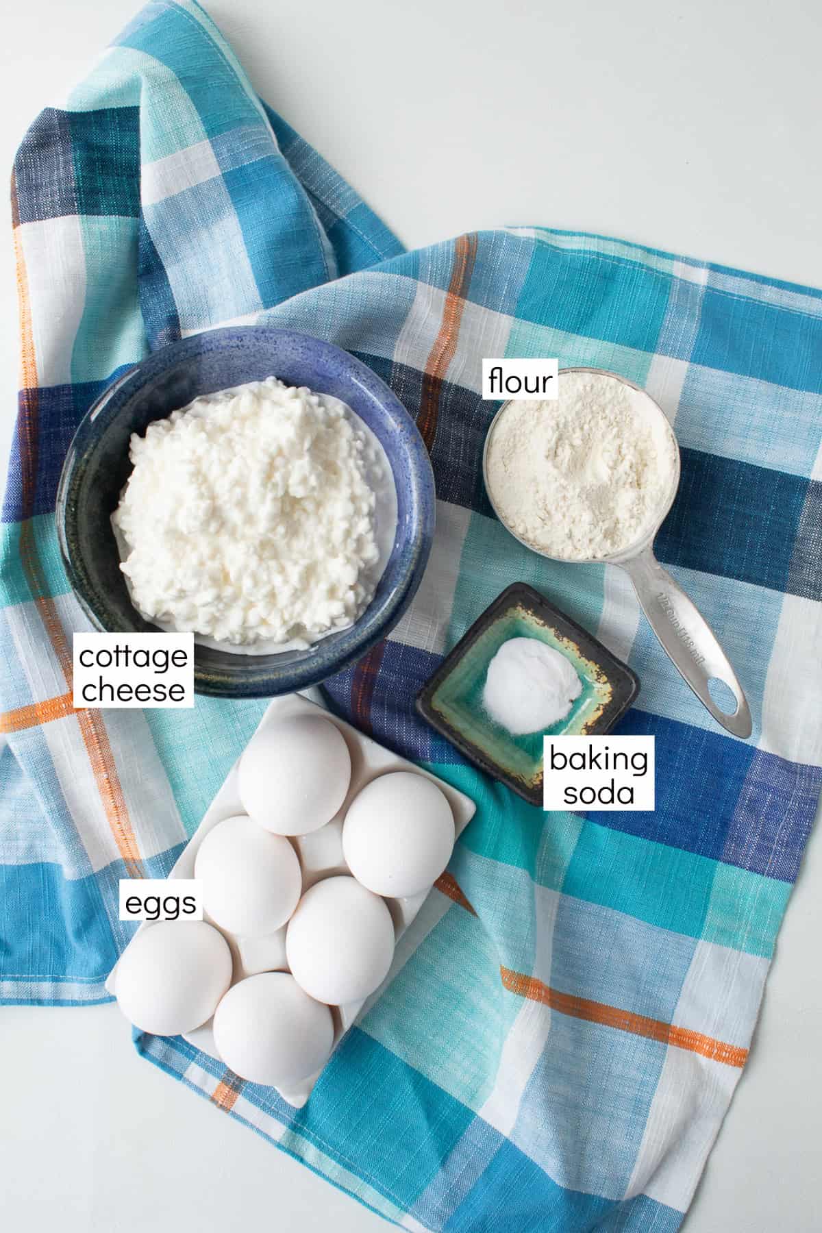 Ingredients for the recipe are displayed on a blue and white background and are labeled with white text boxes including flour, cottage cheese, baking soda, and eggs.