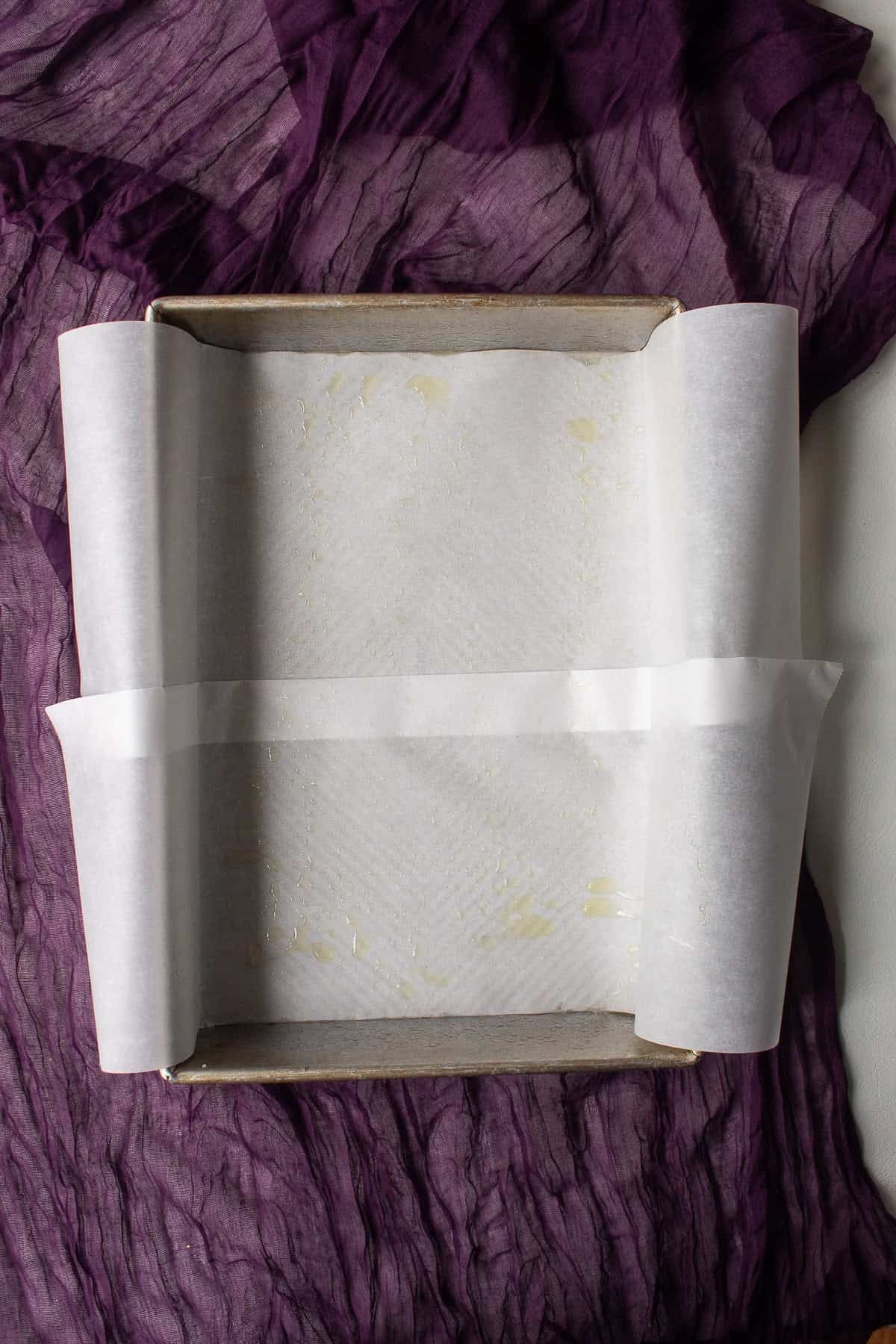 A baking pan is lined with parchment paper and sprayed with cooking spray so that excess parchment can act as a handle to remove the baked bars.
