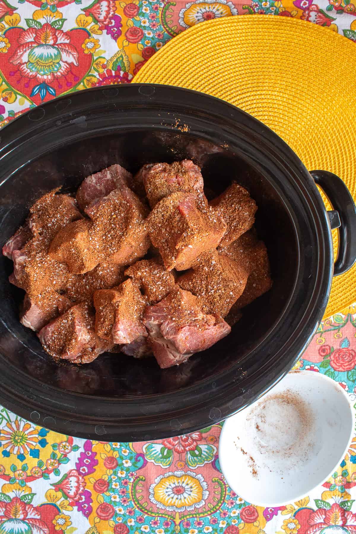 The dry rub spices are sprinkled over the chunks of beef in the slow cooker crock.